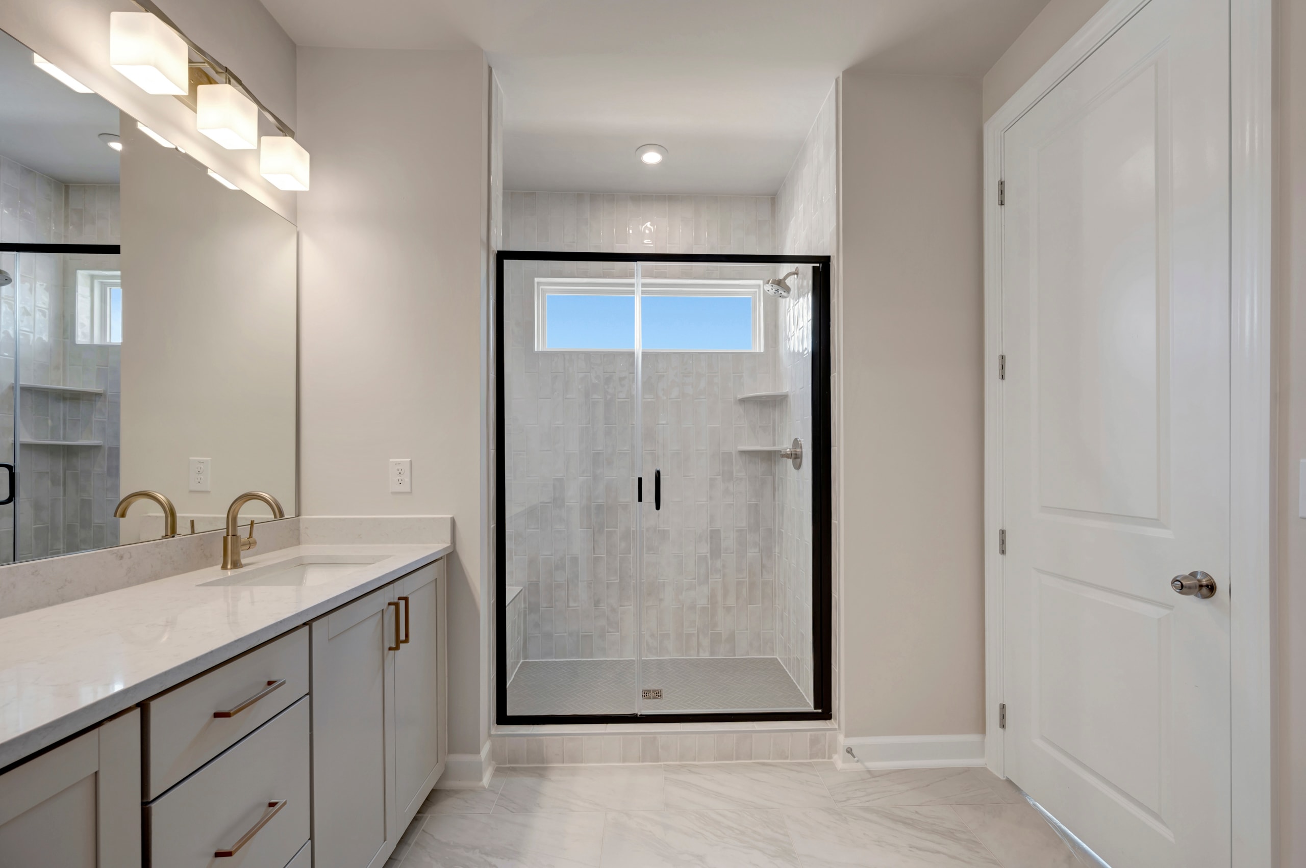 A modern, minimalist bathroom with a large vanity, a glass-enclosed shower, and a window providing natural light.
