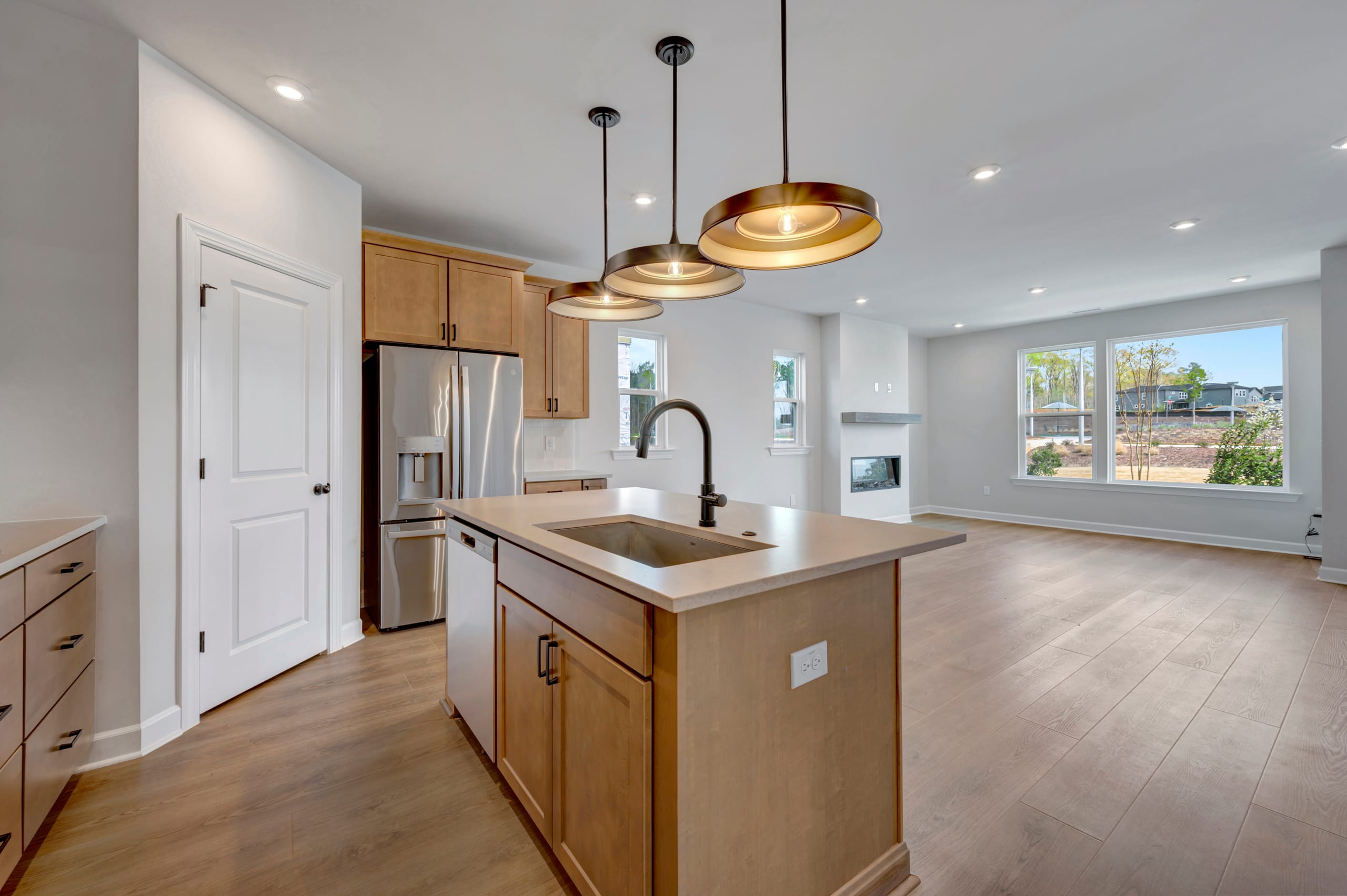 A modern and spacious kitchen with wooden cabinets, stainless steel appliances, and pendant lighting fixtures, set against a backdrop of a bright and airy room with a view of the outdoors.