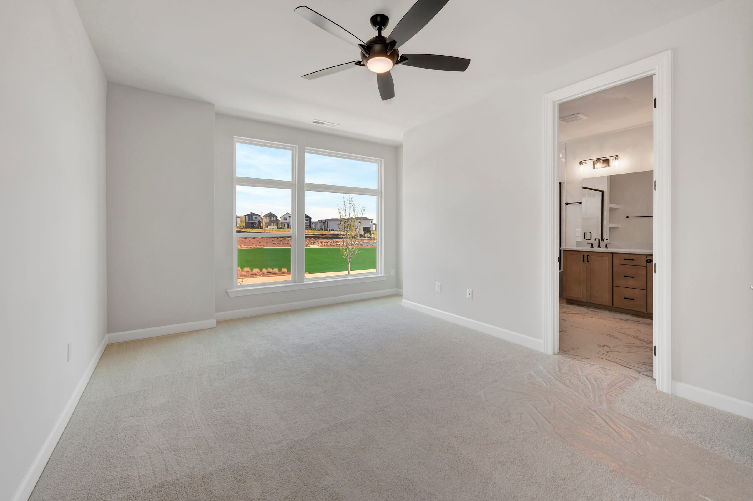 A spacious, well-lit bedroom with a ceiling fan, hardwood floors, and a view of a grassy outdoor area through a large window.