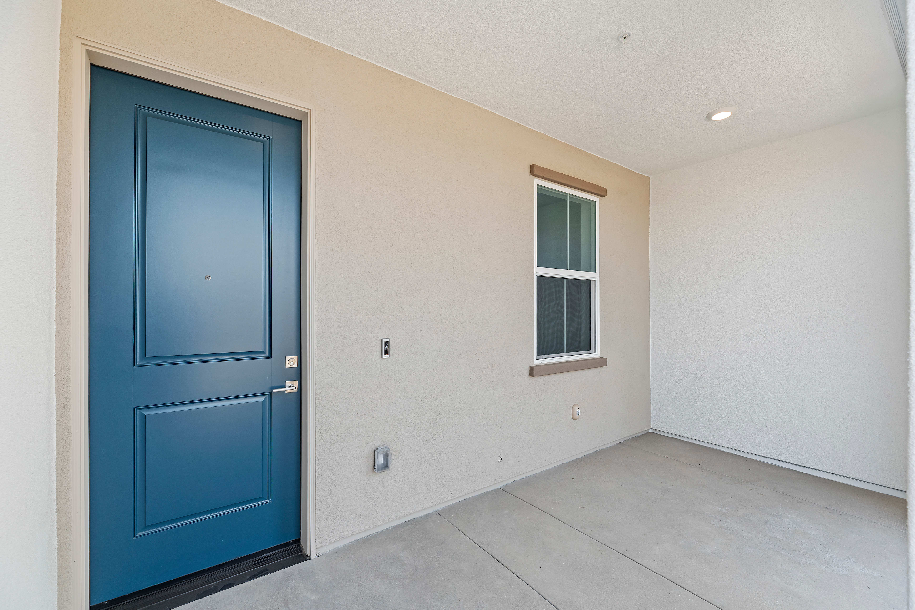 A bright, minimalist room with a blue wooden door and a small window, set against a neutral-colored wall and floor.