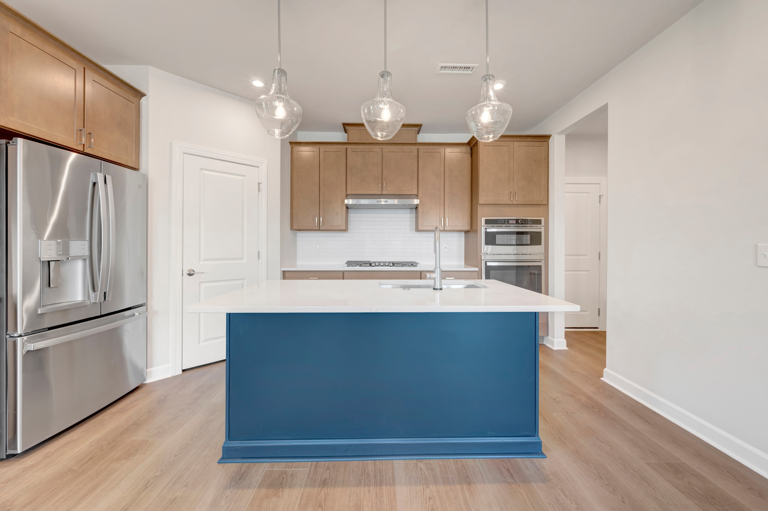 A modern kitchen with a blue island, stainless steel appliances, and pendant lighting fixtures hanging above the island.