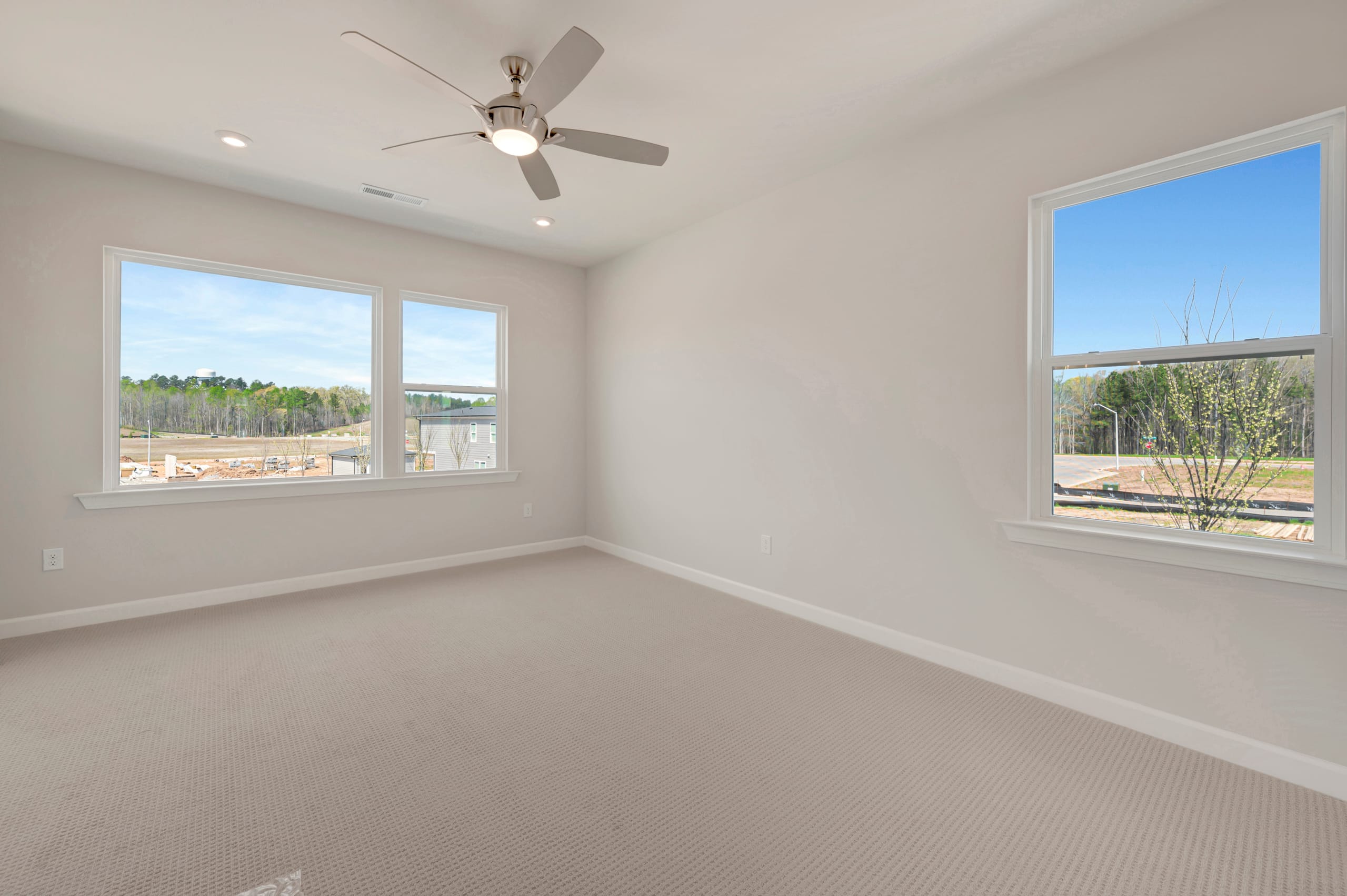 A spacious, well-lit room with a ceiling fan, large windows overlooking a scenic outdoor landscape, and a neutral-toned carpet covering the floor.
