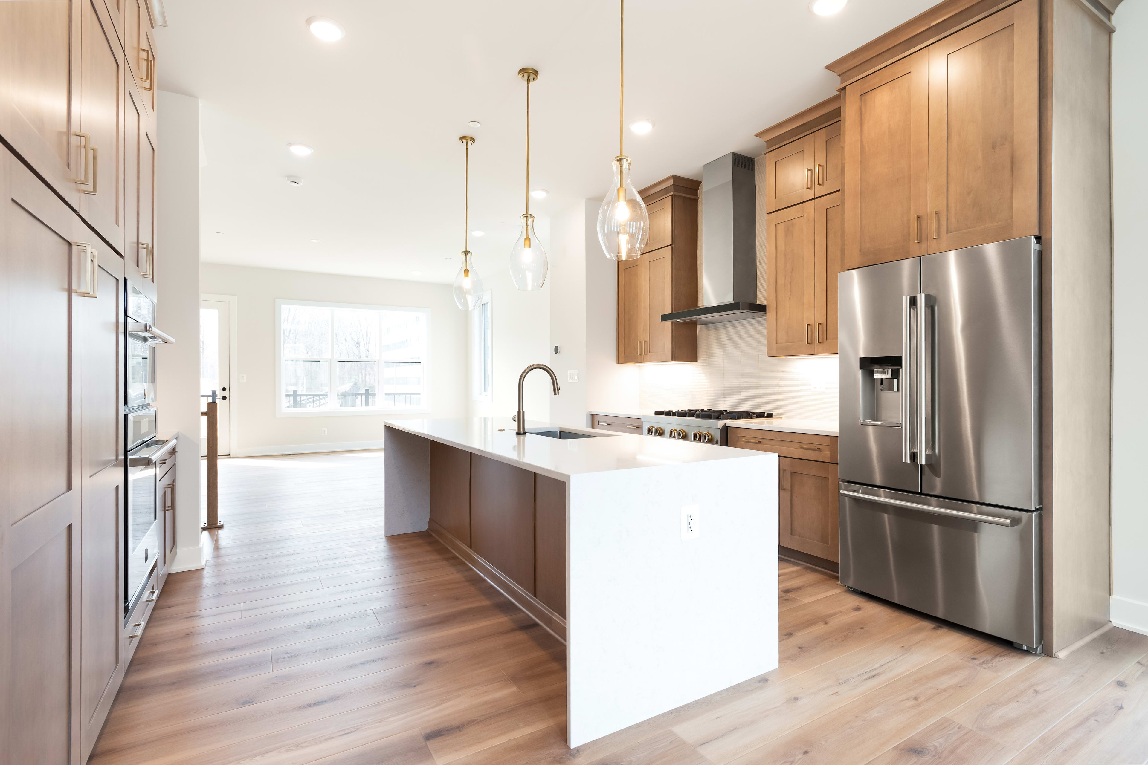A modern, open-concept kitchen with wooden cabinets, stainless steel appliances, and pendant lighting fixtures, set against a bright and airy backdrop.