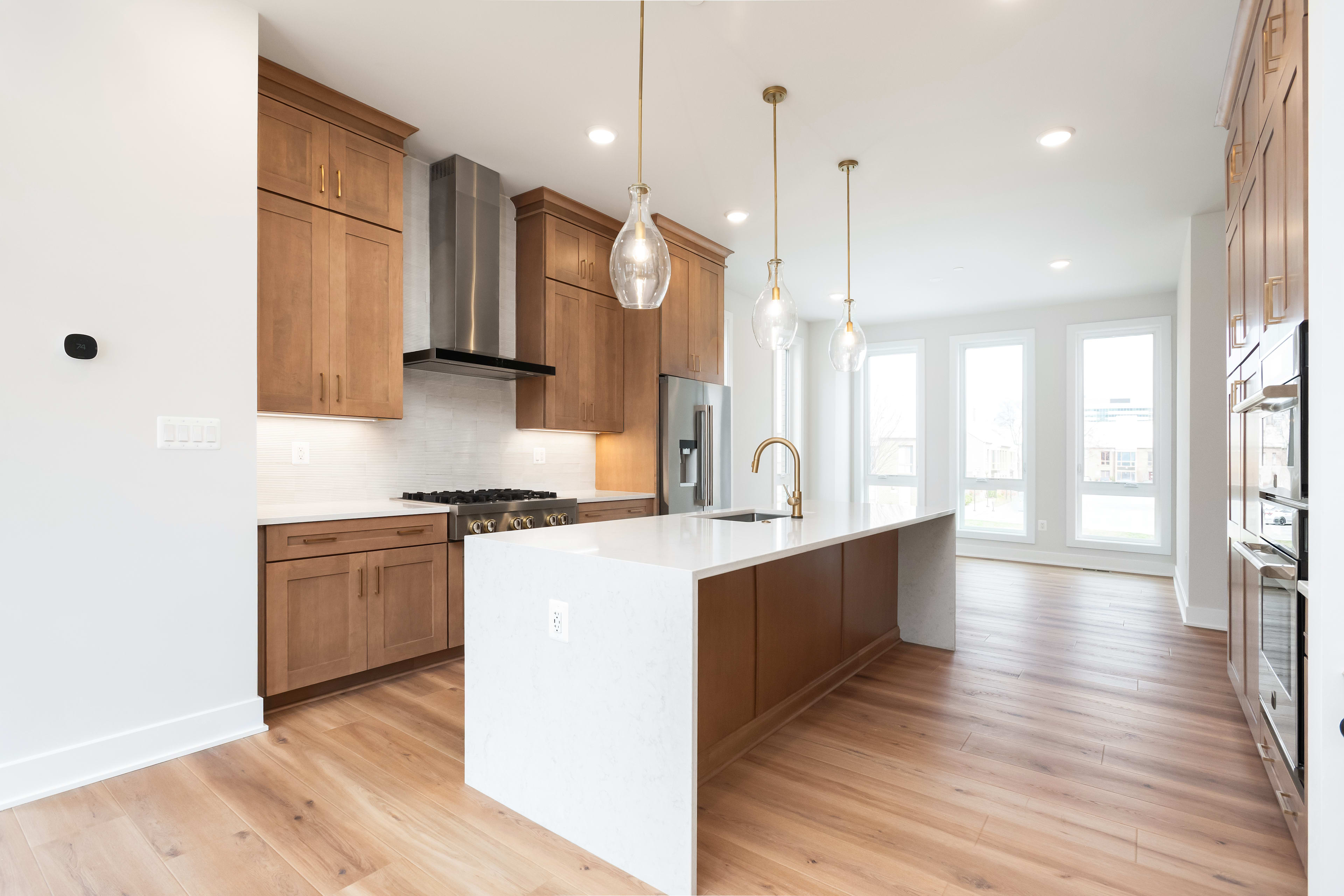 A modern, open-concept kitchen with wooden cabinets, white countertops, and pendant lighting fixtures, leading into a bright and airy living space with hardwood floors.