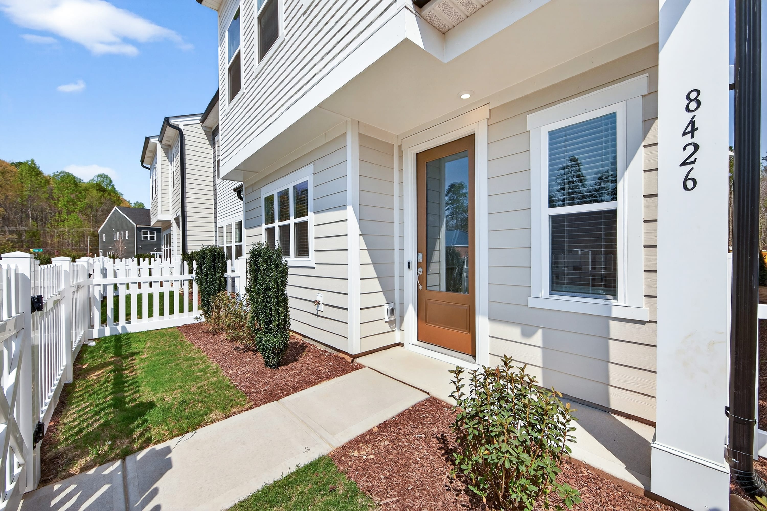 A well-maintained townhouse with a white exterior, a paved walkway, and a small garden in the foreground, set against a backdrop of other similar buildings.