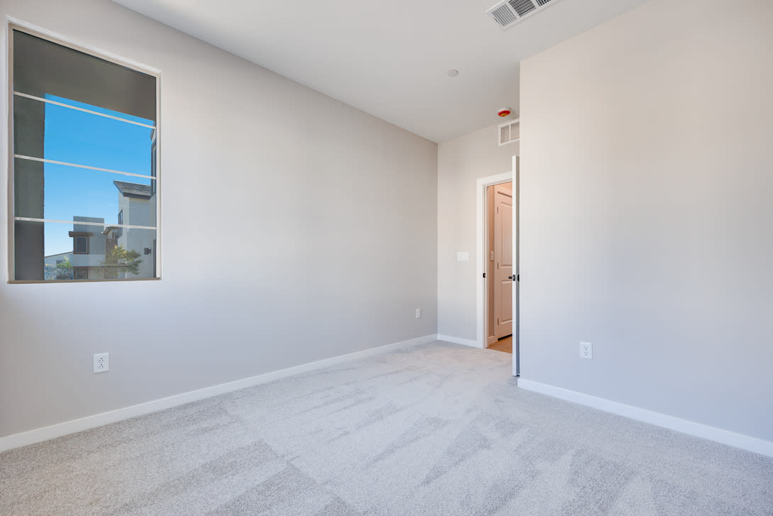 A spacious, well-lit room with a large window overlooking the sky, featuring a clean, minimalist design with white walls and floors.
