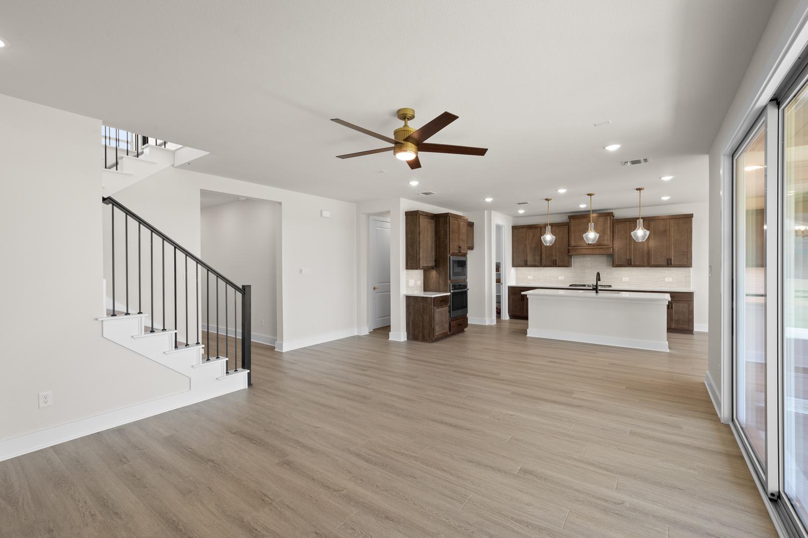 A spacious and modern open-concept living area with a kitchen, dining space, and a staircase leading to an upper level. The room features hardwood floors, a ceiling fan, and large windows providing ample natural light.
