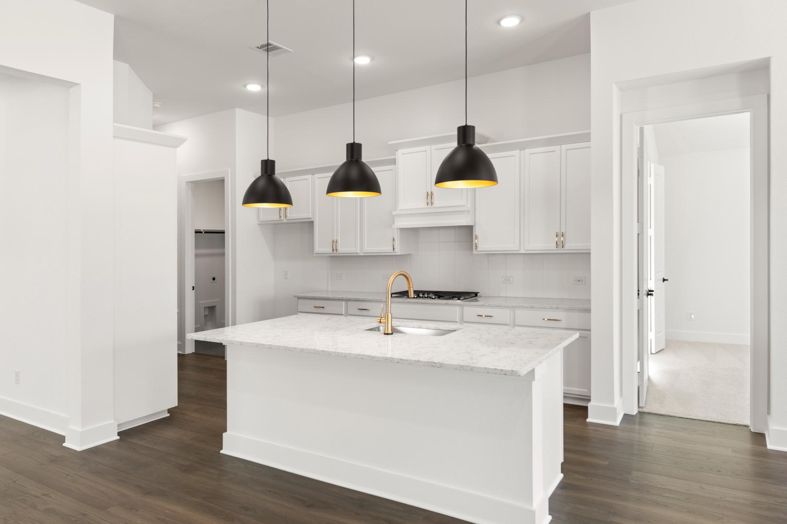 A modern, minimalist kitchen with white cabinets, a large central island, and three black pendant lights hanging above the island.