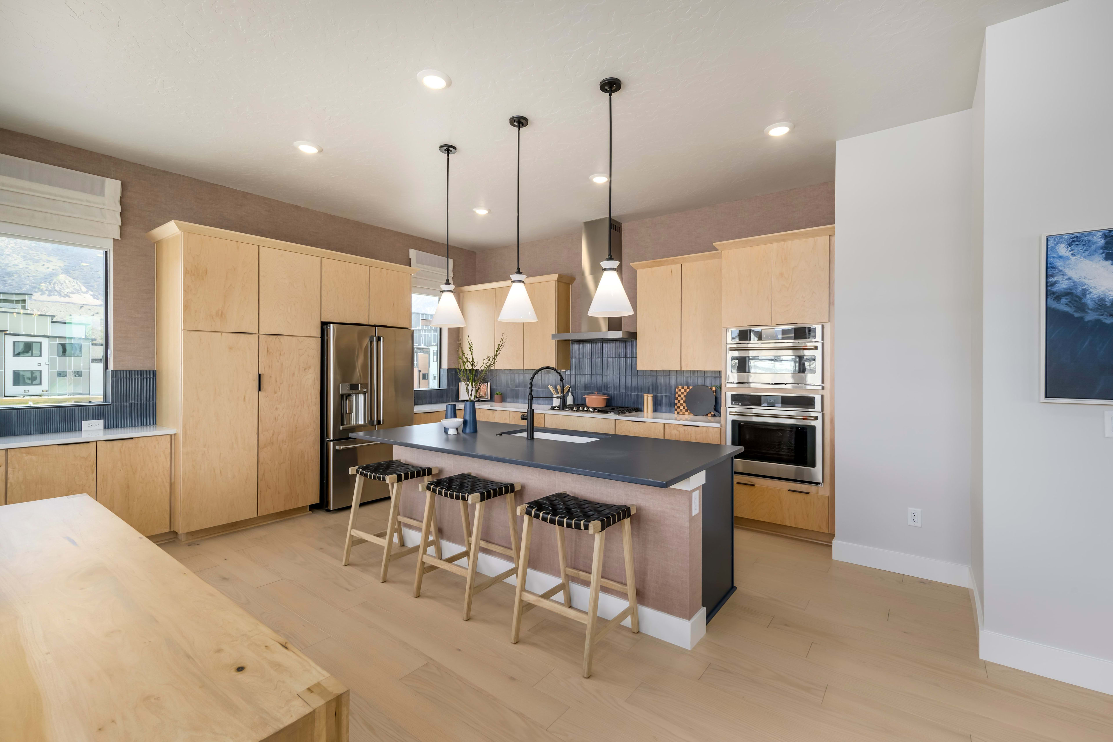 A modern and spacious kitchen with light-colored wood cabinets, a large island with bar stools, and pendant lights hanging from the ceiling.