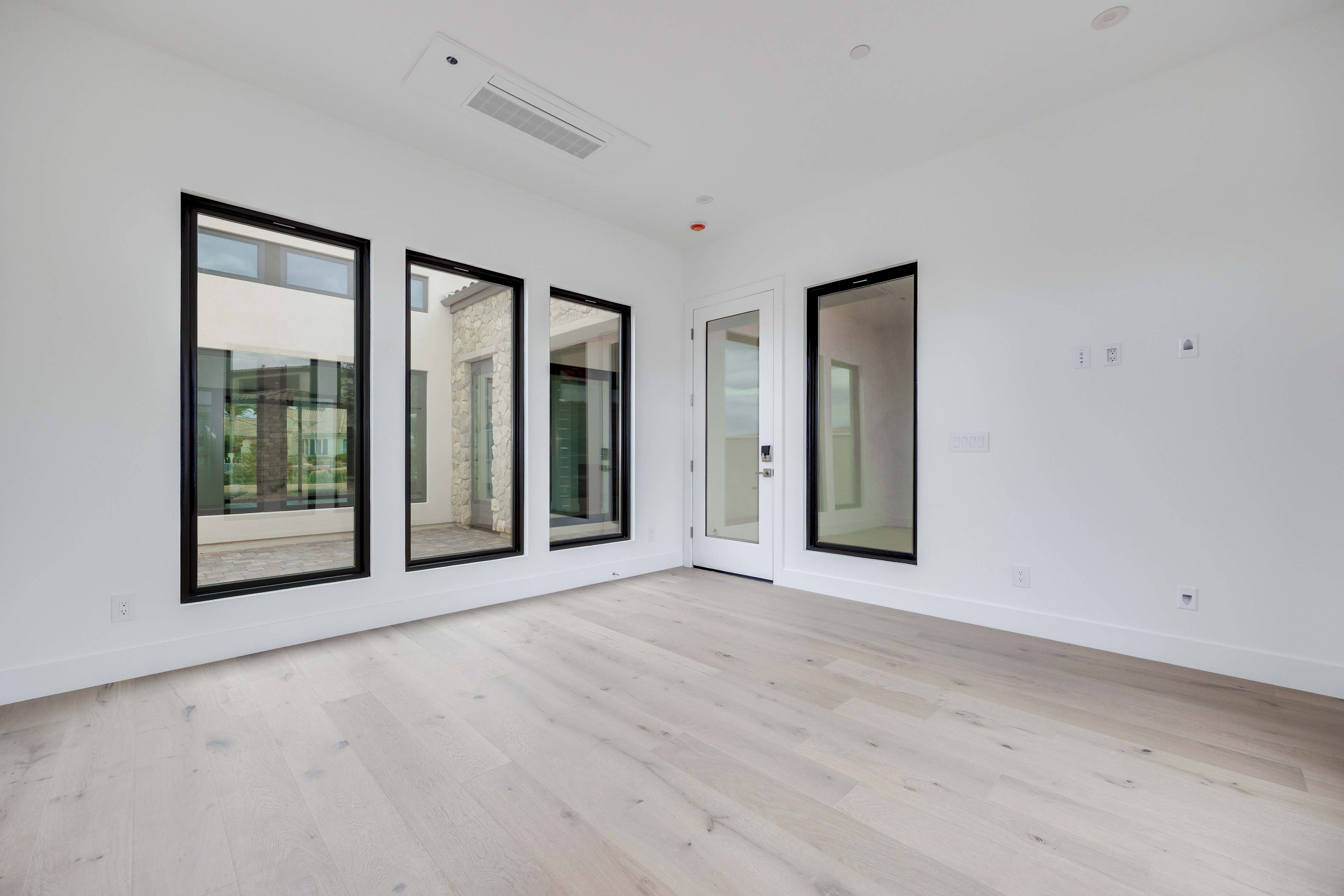 A spacious, minimalist room with large windows and a hardwood floor, creating a bright and airy atmosphere.