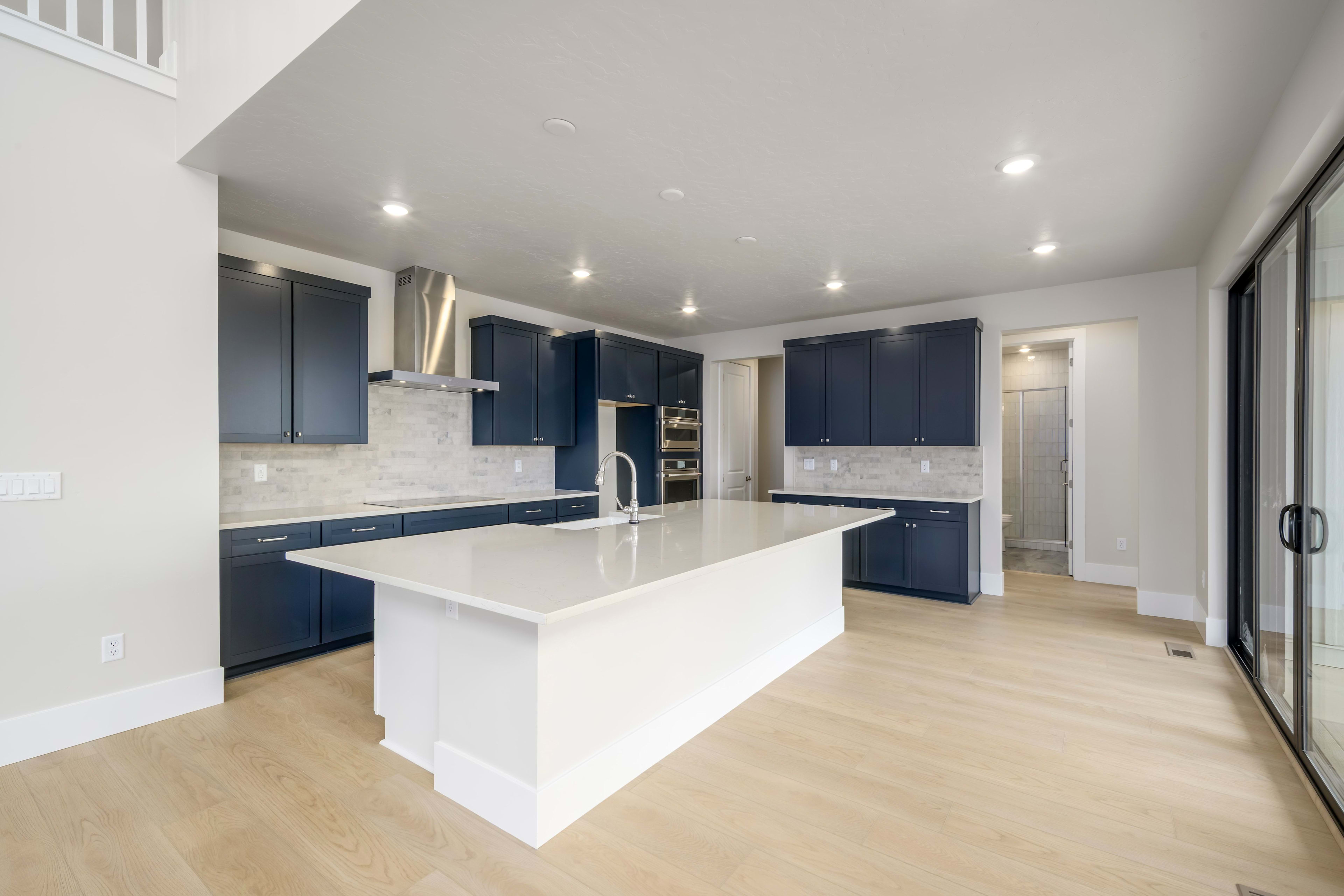 A modern, open-concept kitchen with navy blue cabinets, a white island, and hardwood floors.