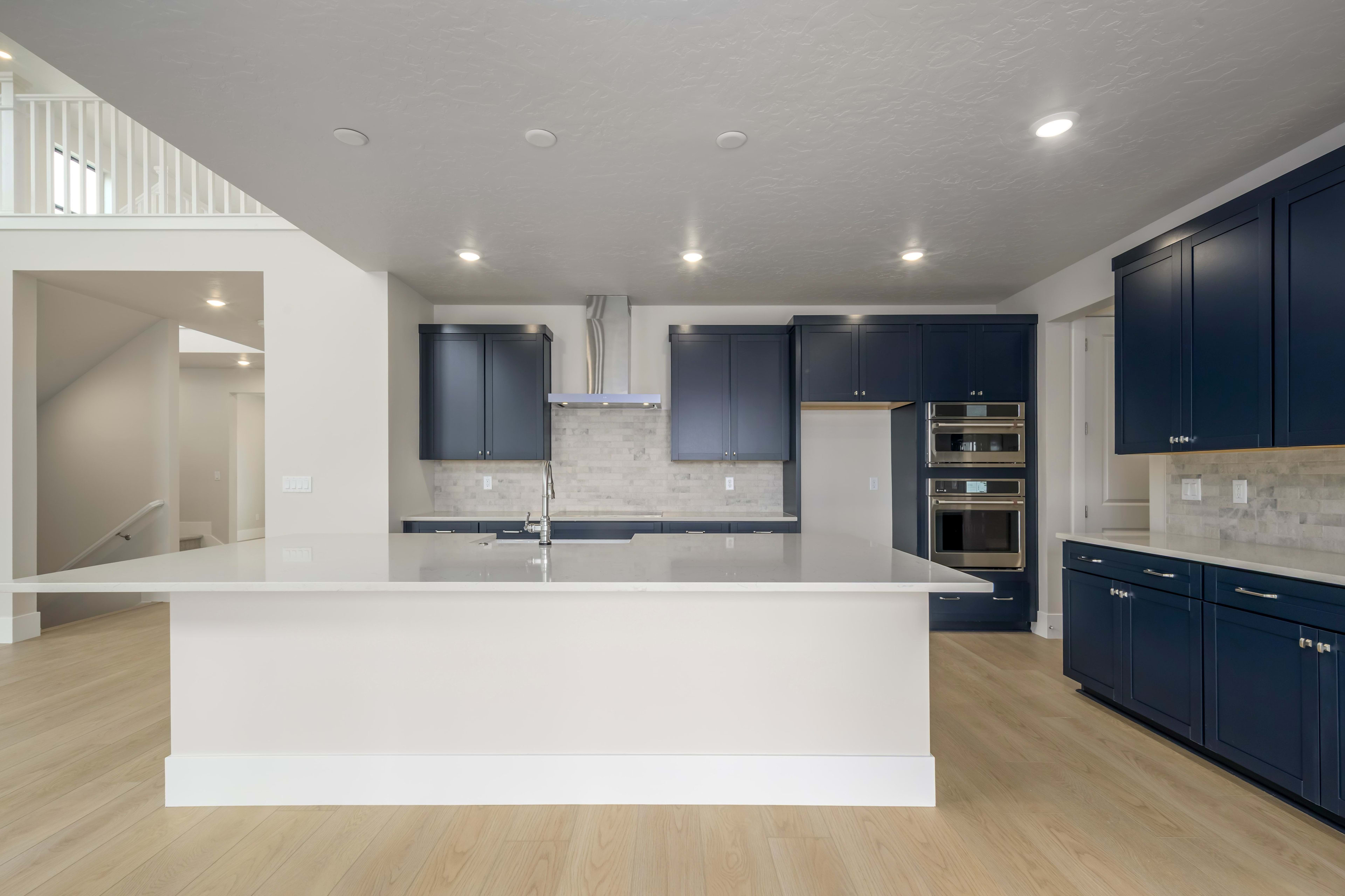A modern, open-concept kitchen with a white island countertop, dark blue cabinets, and stainless steel appliances, set against a light-colored hardwood floor.