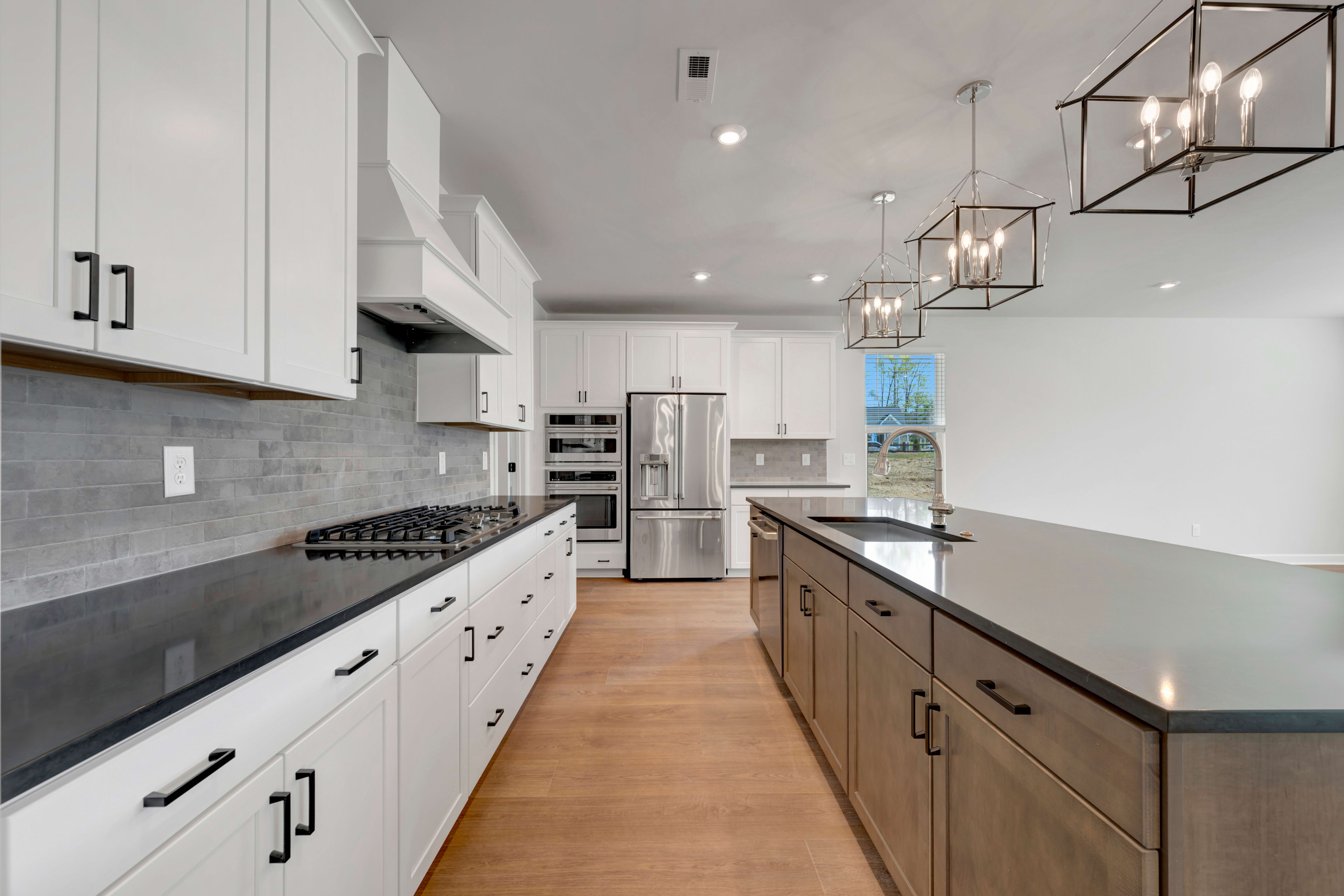 A modern, well-lit kitchen with white cabinets, stainless steel appliances, and a long wooden countertop running along the center of the room.
