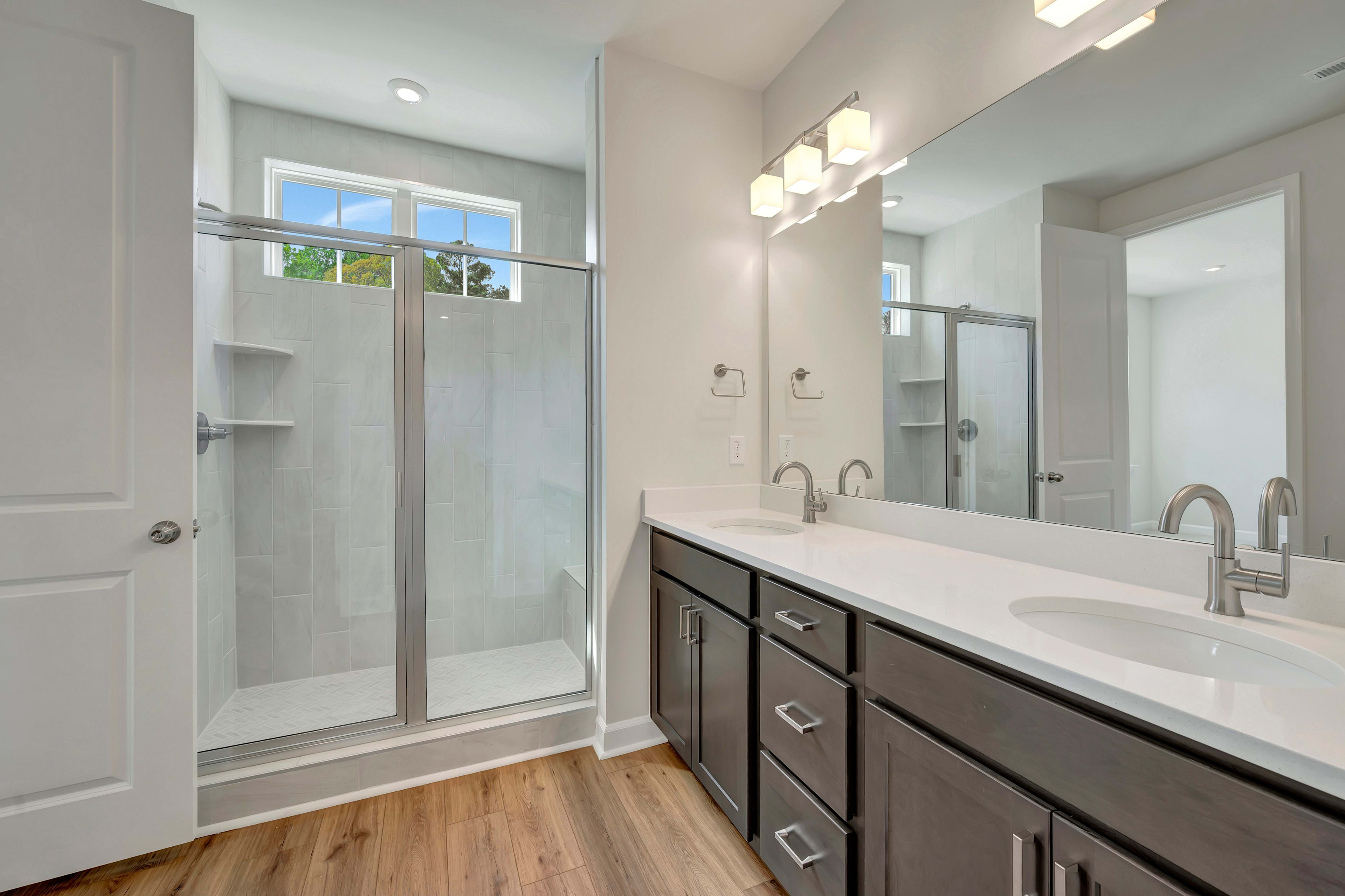 A modern bathroom with a vanity, sink, and a glass-enclosed shower area, featuring hardwood flooring and recessed lighting.
