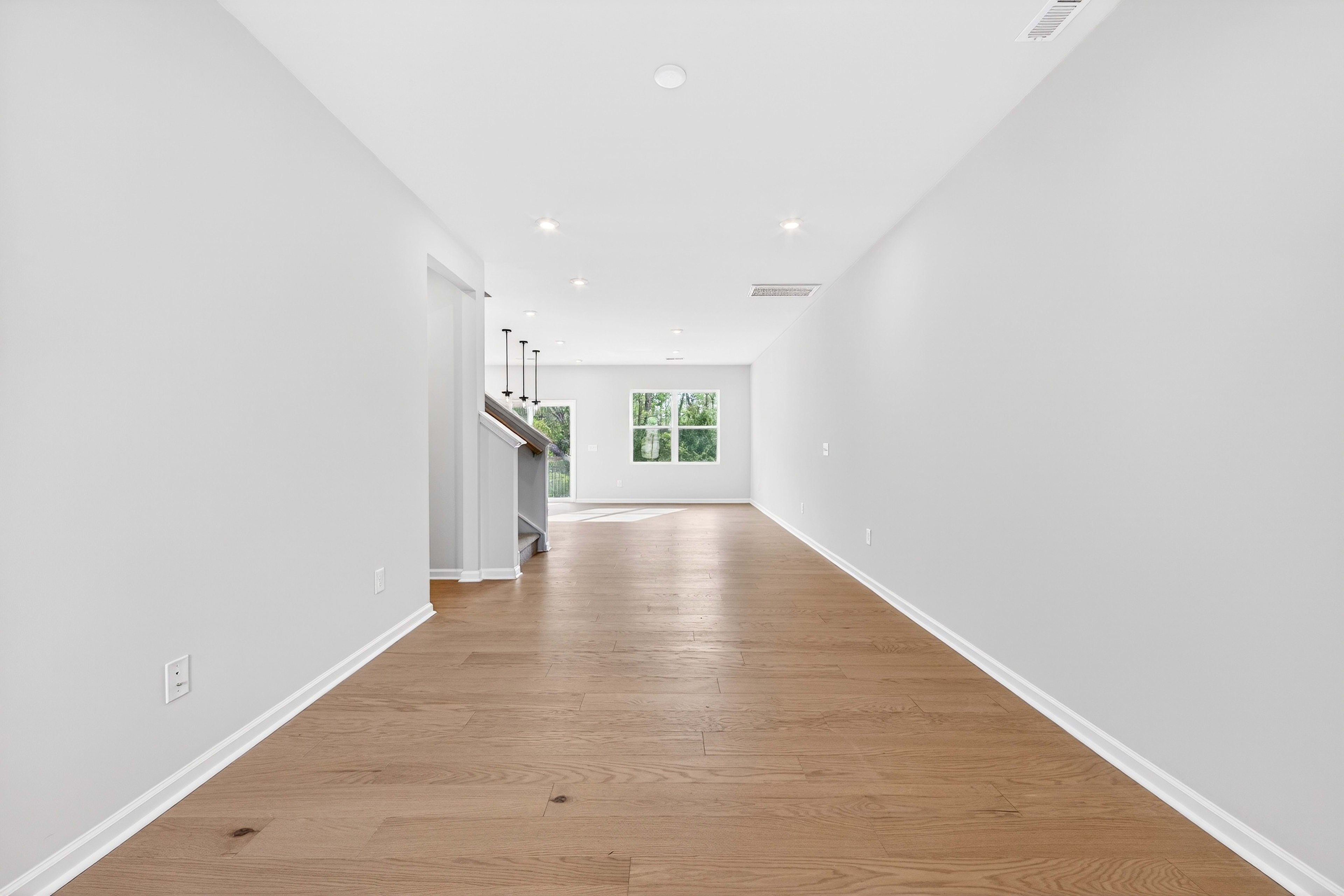 A long, bright hallway with white walls and a wooden floor, leading to a window at the end.