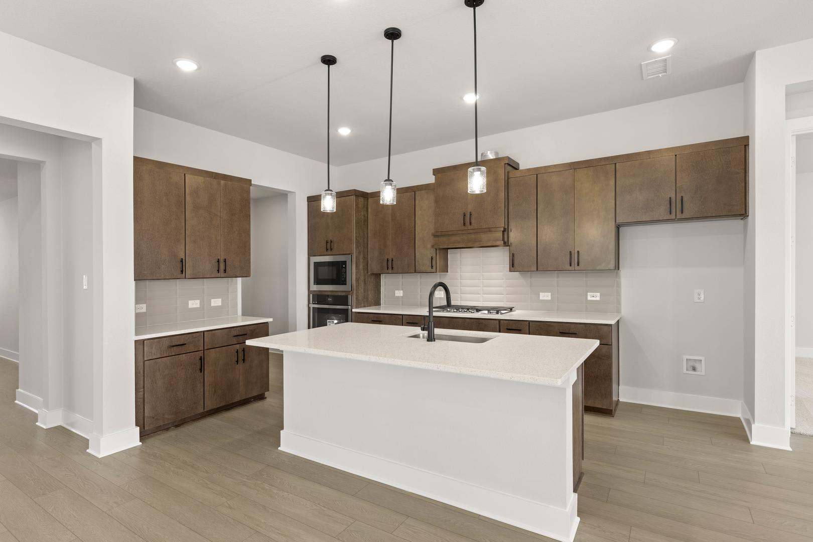 A modern, open-concept kitchen with white countertops, wooden cabinets, and pendant lighting fixtures, set against a backdrop of a bright, airy space.