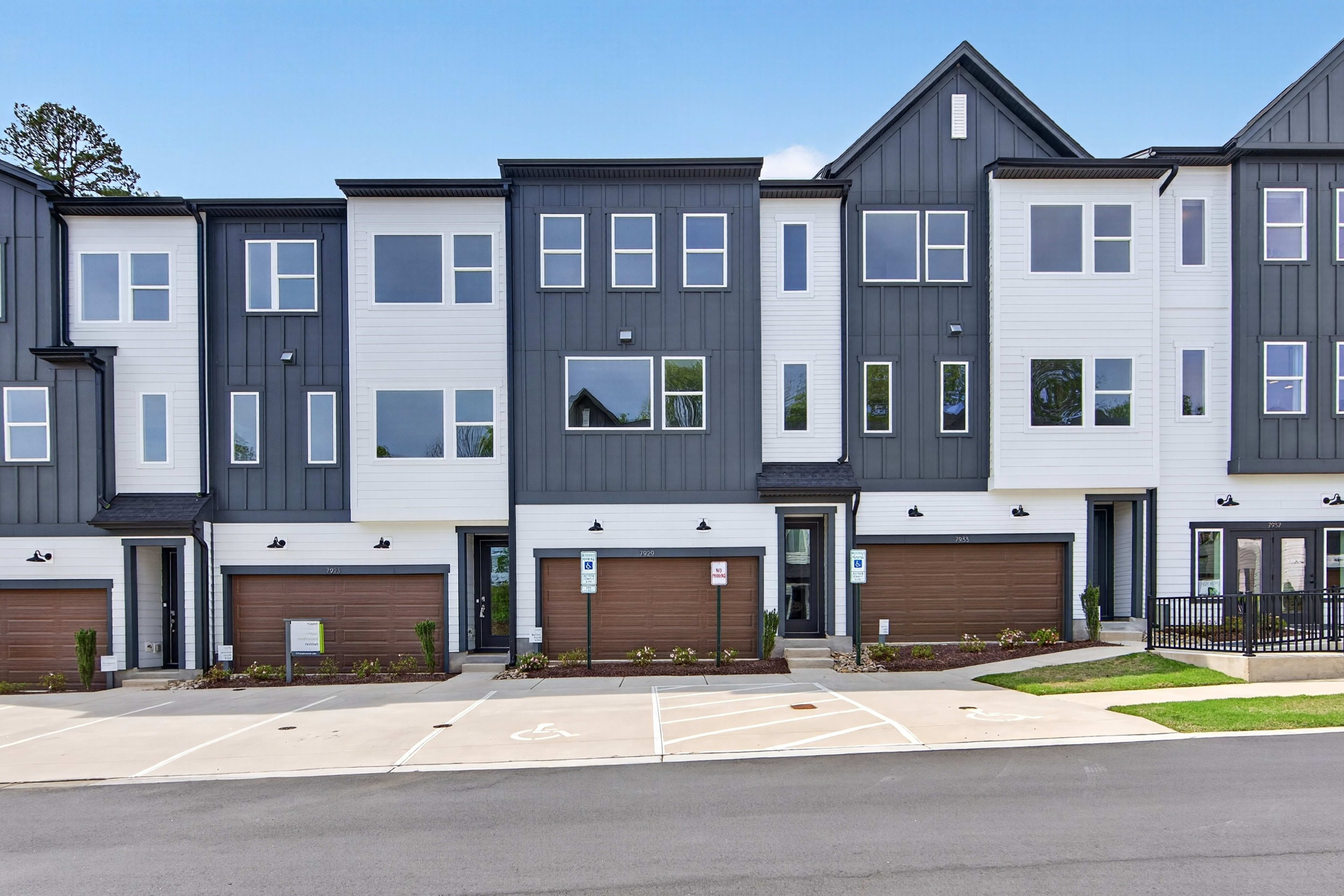 A row of modern, multi-story townhouses with a mix of gray and brown siding, large windows, and attached garages, set against a clear blue sky.