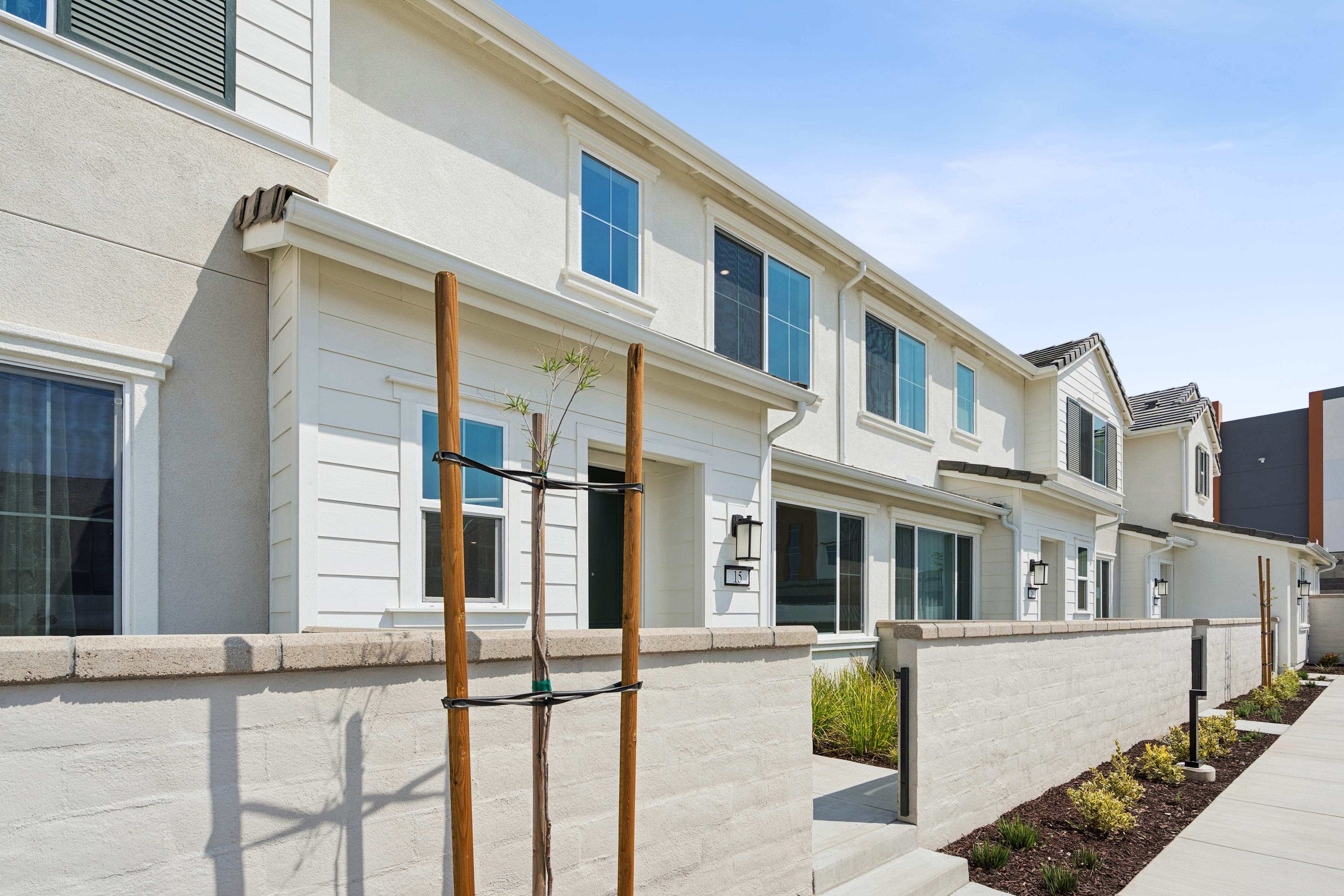 A modern, multi-story residential building with a clean, minimalist design, surrounded by landscaped greenery and a paved walkway in the foreground.