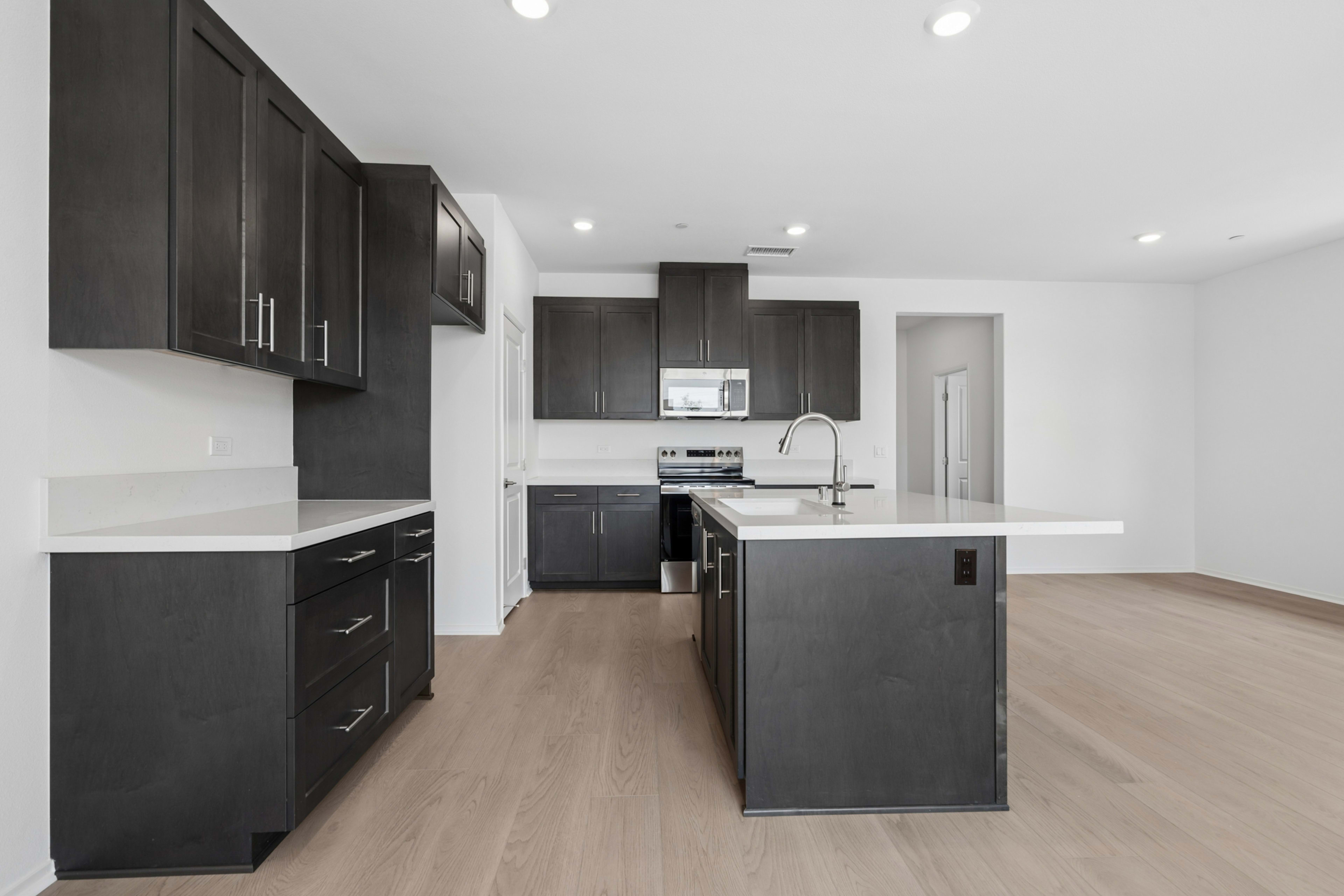 A modern kitchen with dark cabinets, a white countertop, and a hardwood floor.