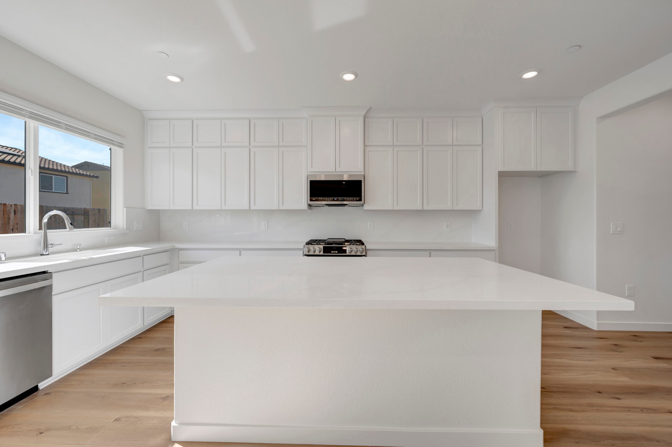 A modern, minimalist kitchen with white cabinets, a large island, and hardwood floors, set against a bright and airy background.