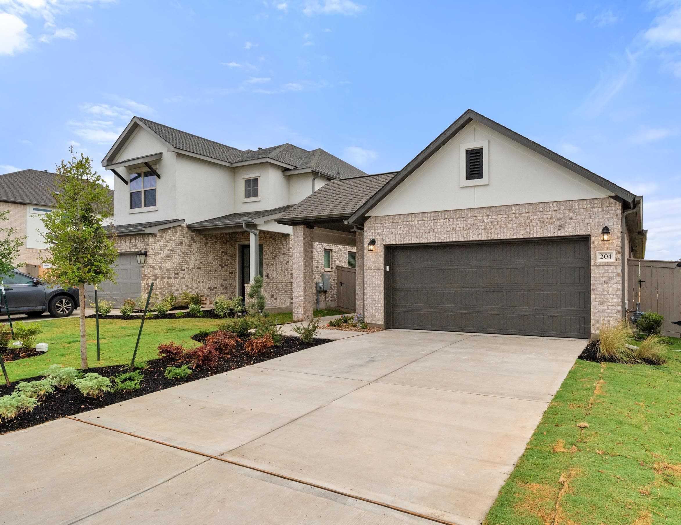 A two-story residential house with a brick exterior, a garage, and a well-maintained lawn in the foreground.