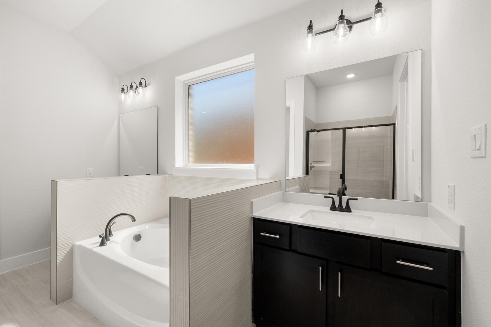 A modern and minimalist bathroom with a white bathtub, a black vanity cabinet, and a large window providing natural light.