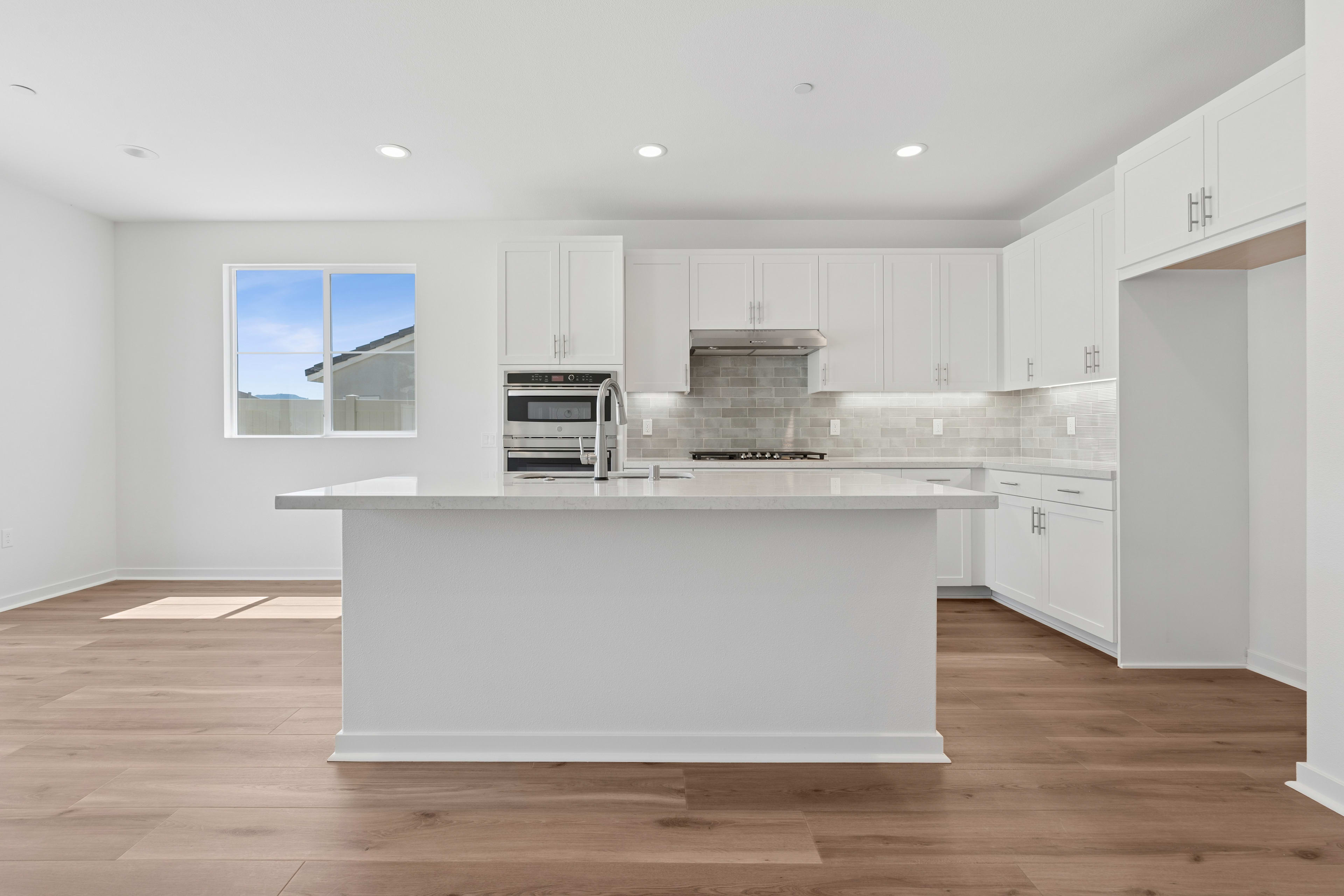 A modern, open-concept kitchen with white cabinets, a large island, and hardwood floors, set against a bright, airy backdrop.