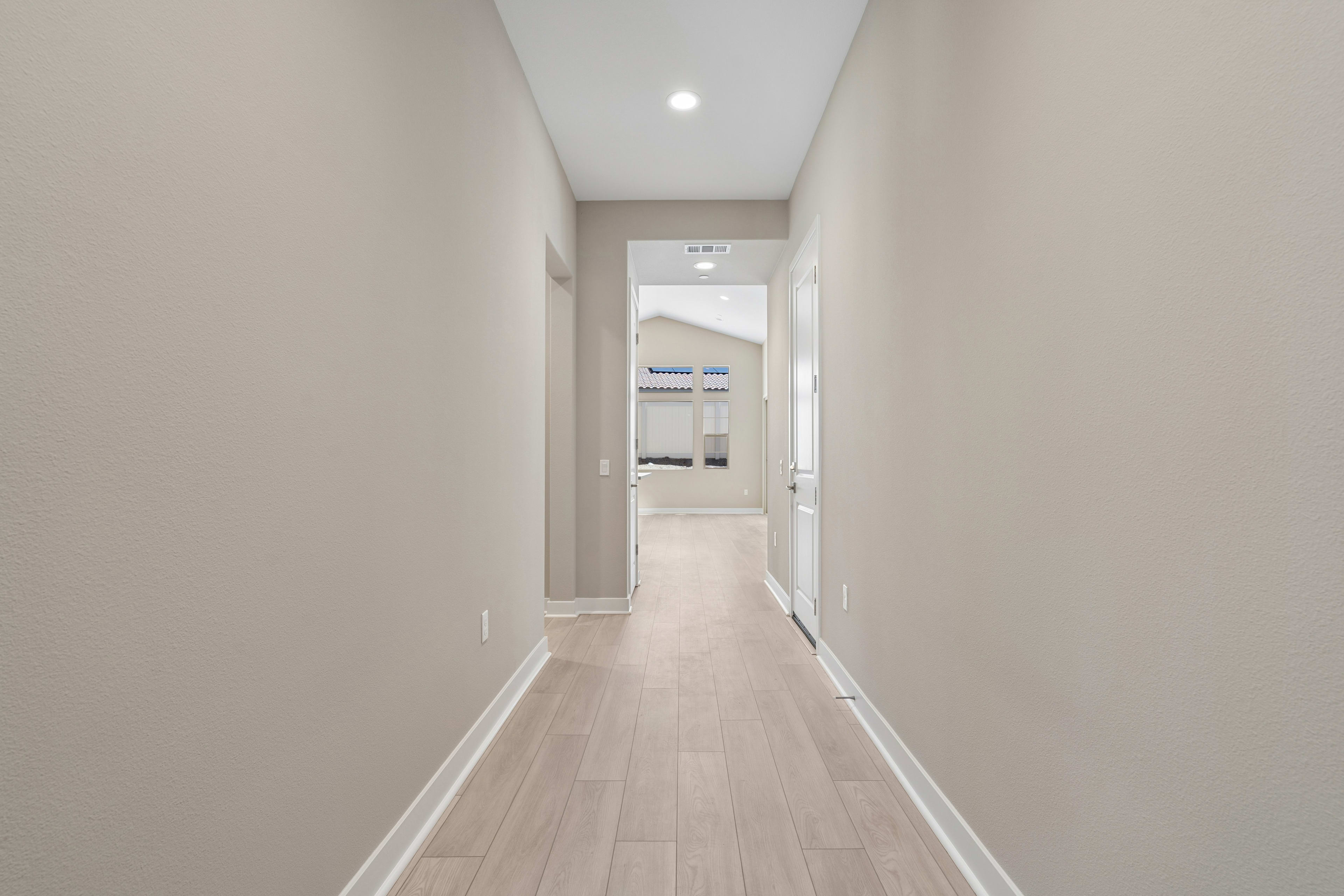 A long, narrow hallway with light-colored walls and a wooden floor extends into the distance, leading to a partially visible doorway.