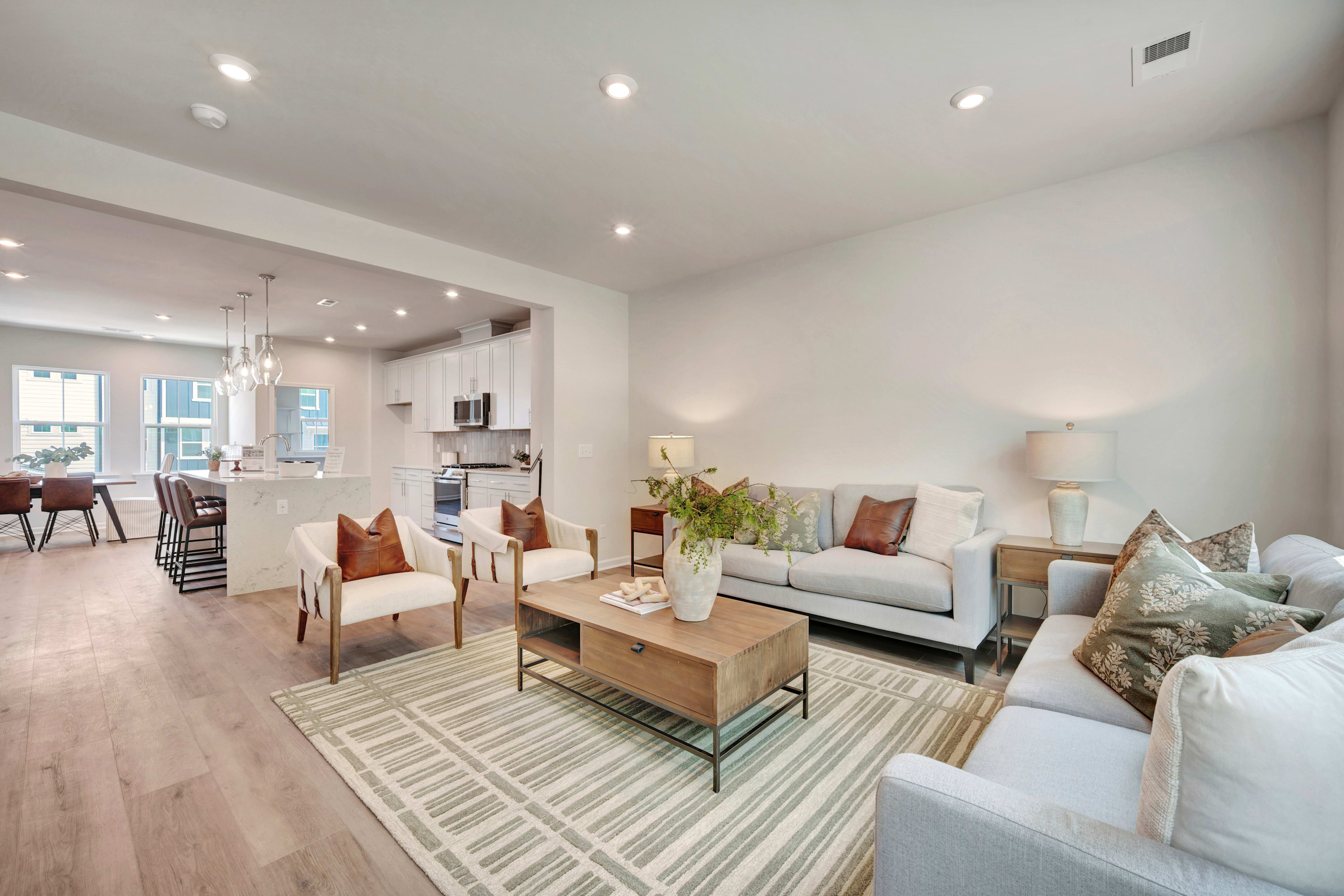 A modern and cozy living room with a comfortable sofa, armchairs, and a coffee table on a patterned rug, surrounded by white walls and recessed lighting.