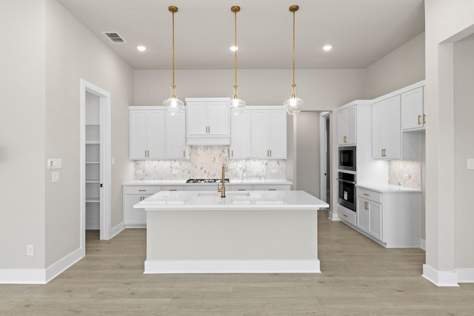 A modern, bright, and spacious kitchen with white cabinets, a marble-topped island, and gold pendant lights.