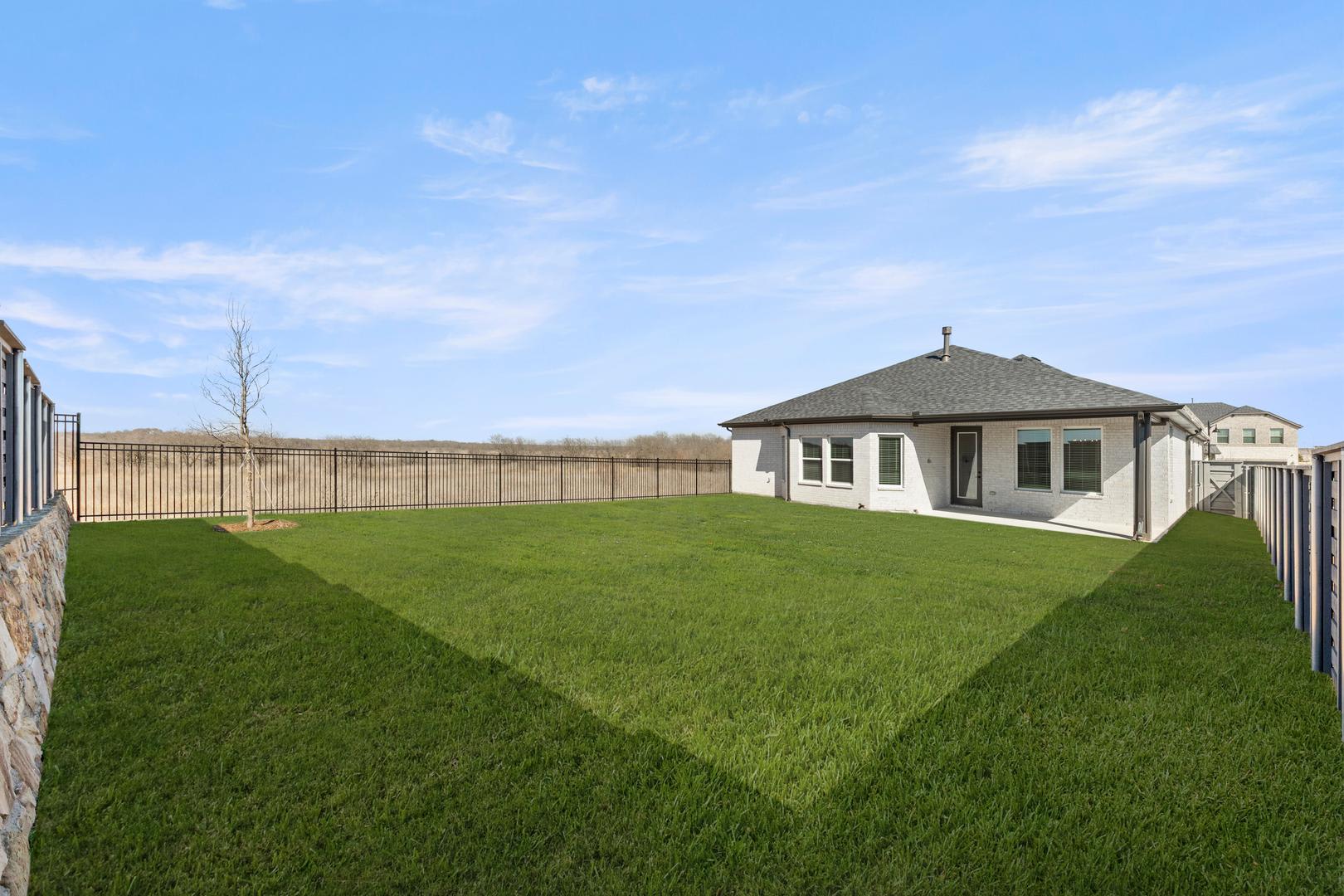 A well-manicured lawn surrounds a small, single-story house with a peaked roof, set against a clear blue sky with wispy clouds.