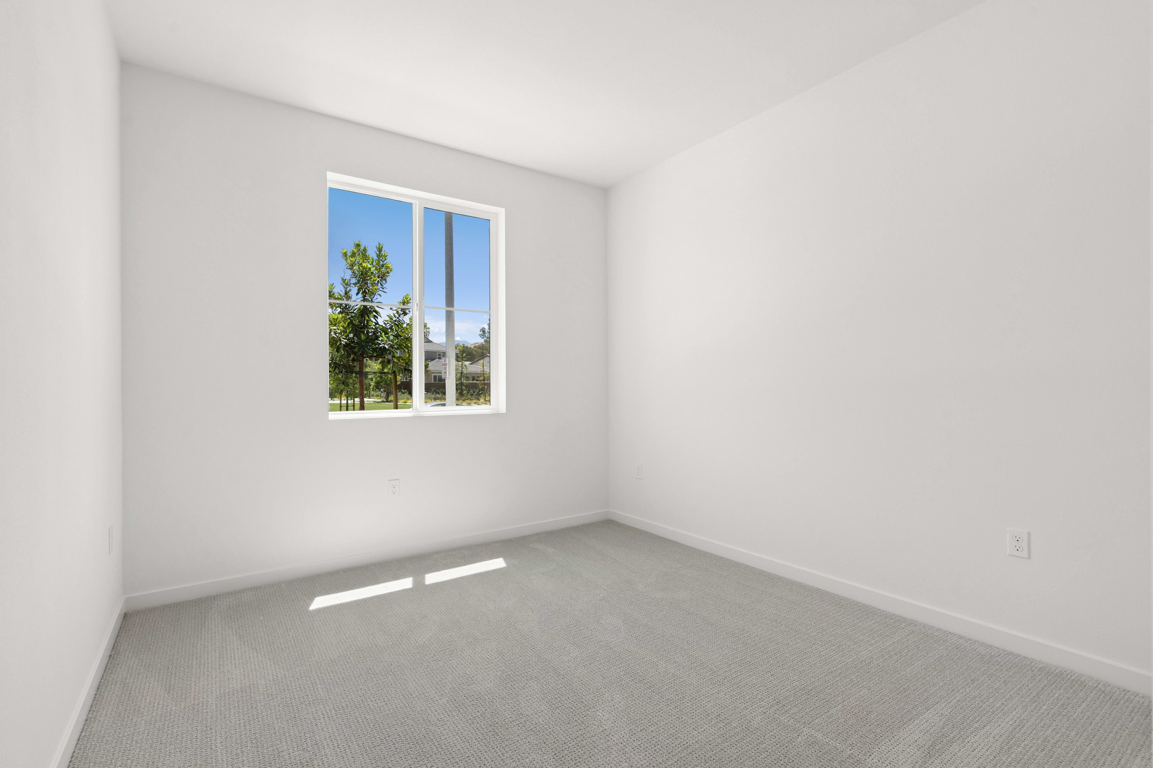 A bright, empty room with a large window overlooking a lush, green outdoor area.