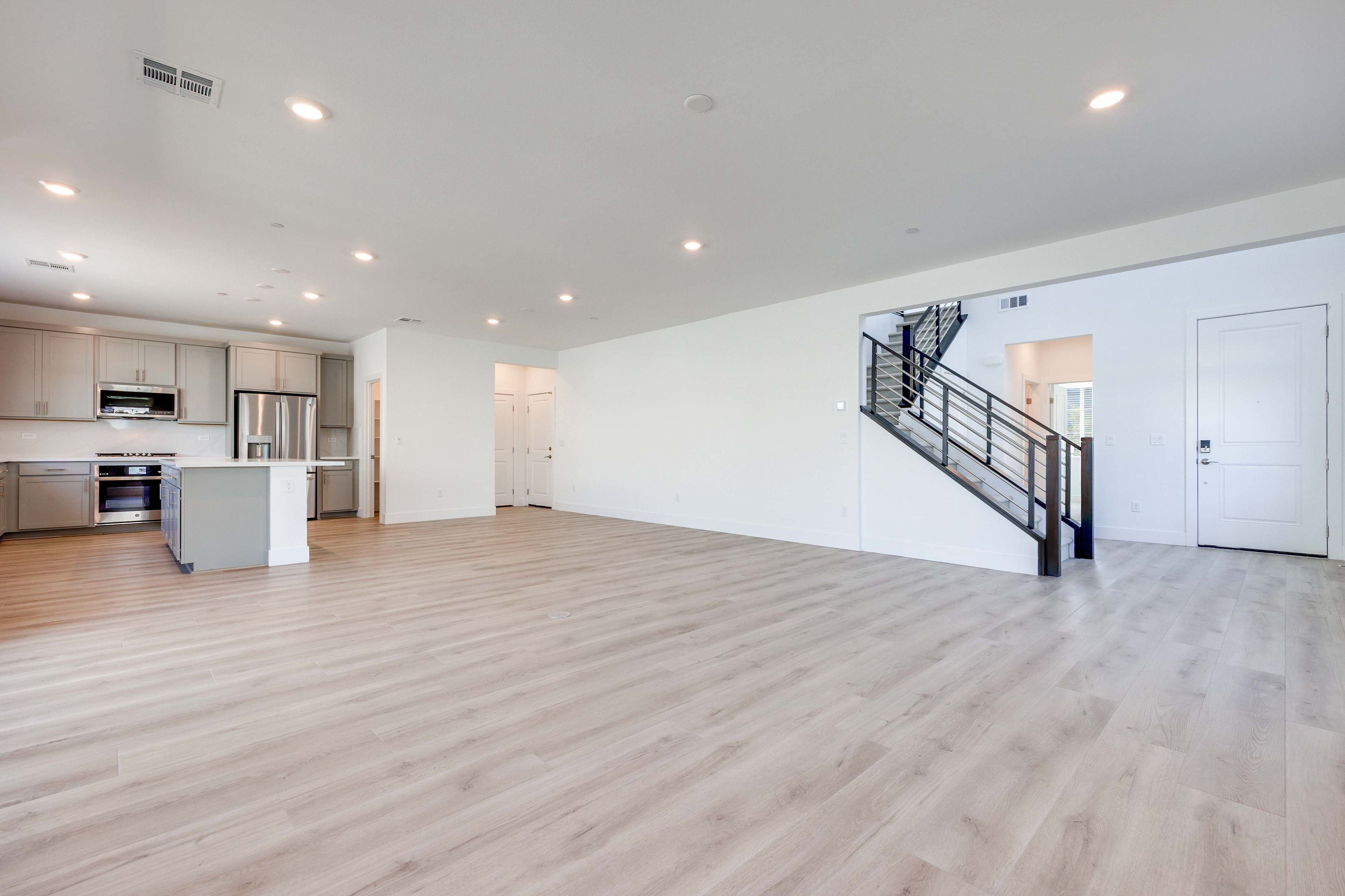 A spacious, open-concept living area with a modern kitchen, hardwood floors, and a staircase leading to an upper level.