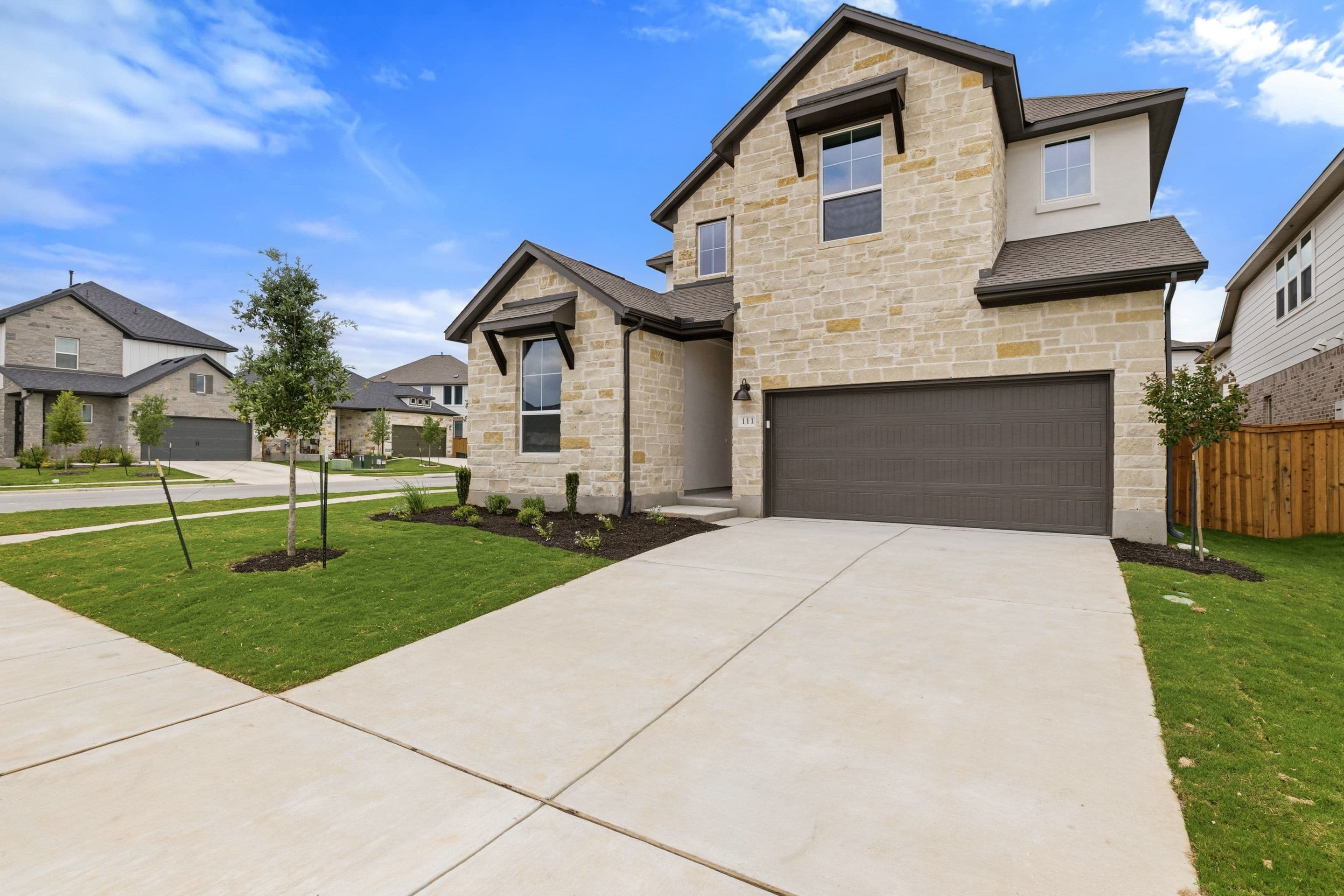 A two-story residential house with a stone exterior, a garage, and a well-maintained lawn in a suburban neighborhood setting.