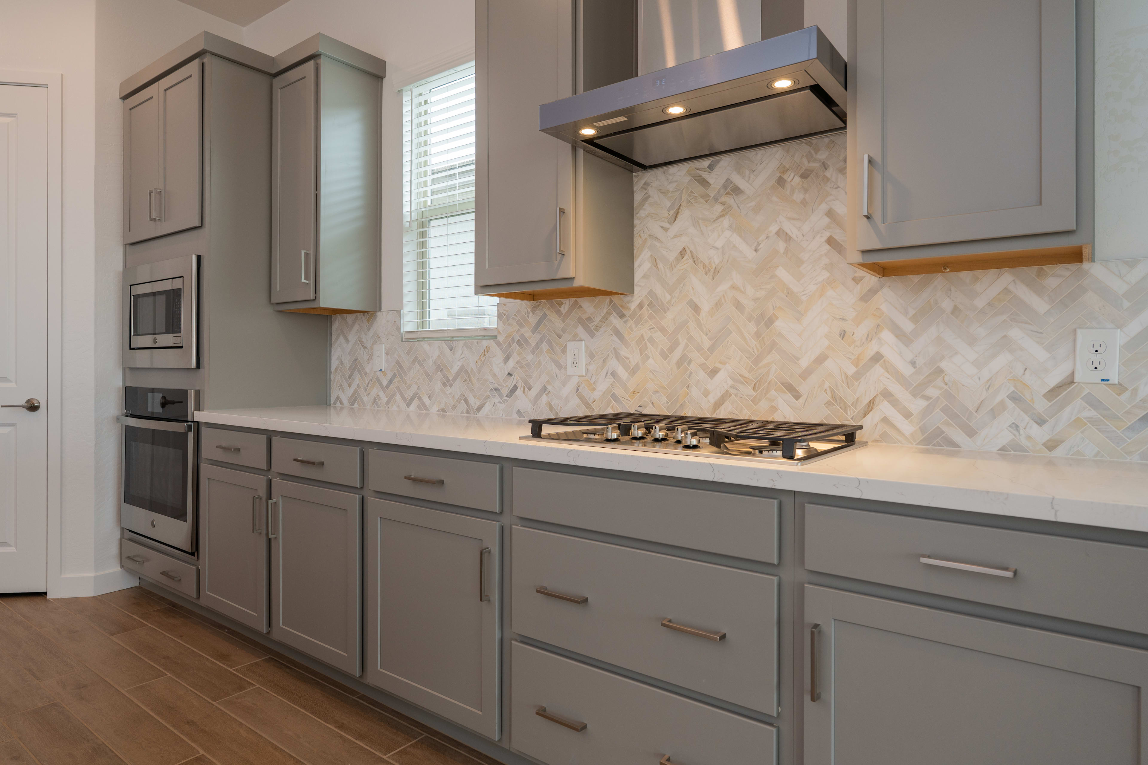A modern kitchen with gray cabinets, a herringbone tile backsplash, and a gas stove top.