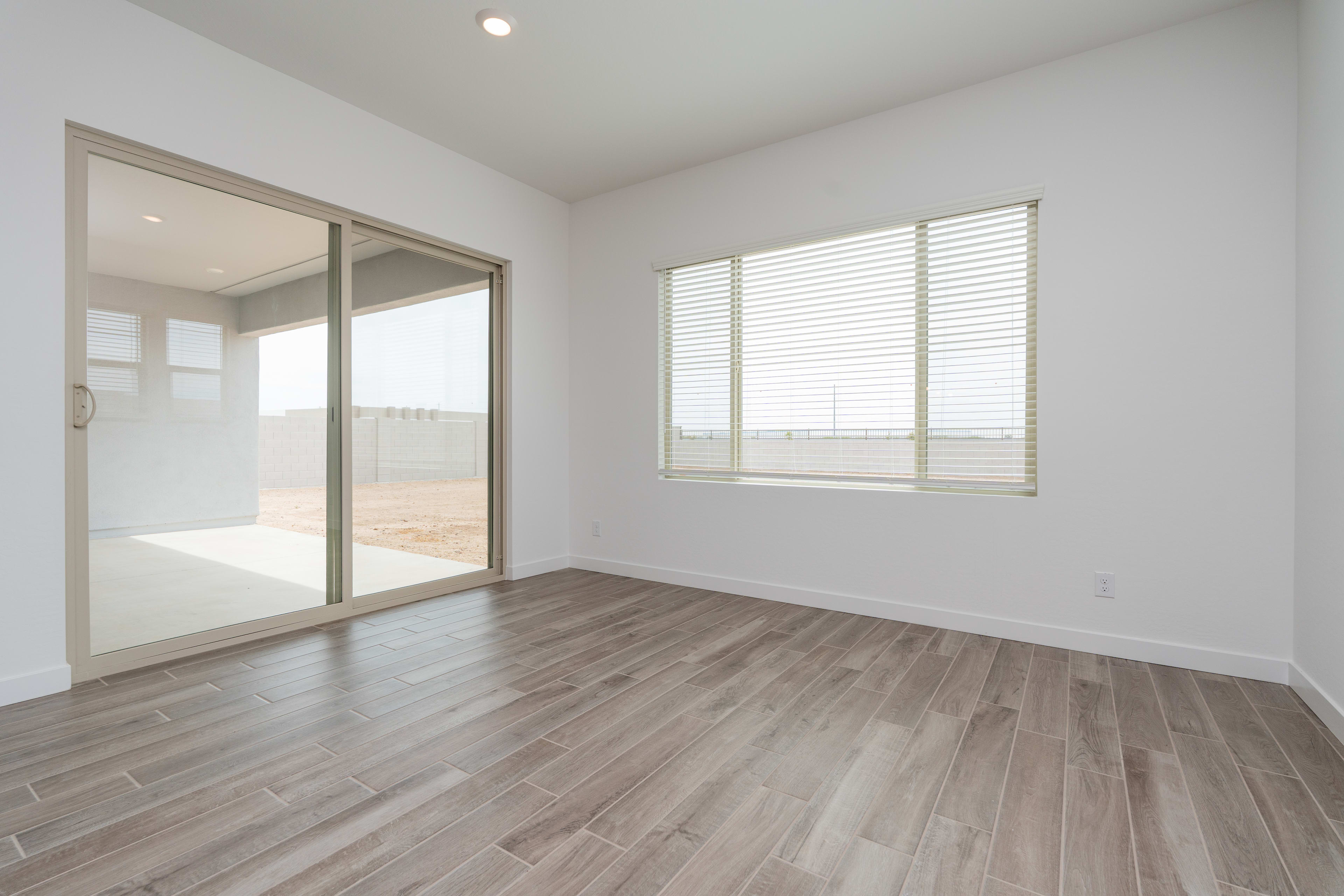 A spacious, well-lit room with a sliding glass door leading to an outdoor area, featuring a hardwood-style floor and a large window providing natural light.
