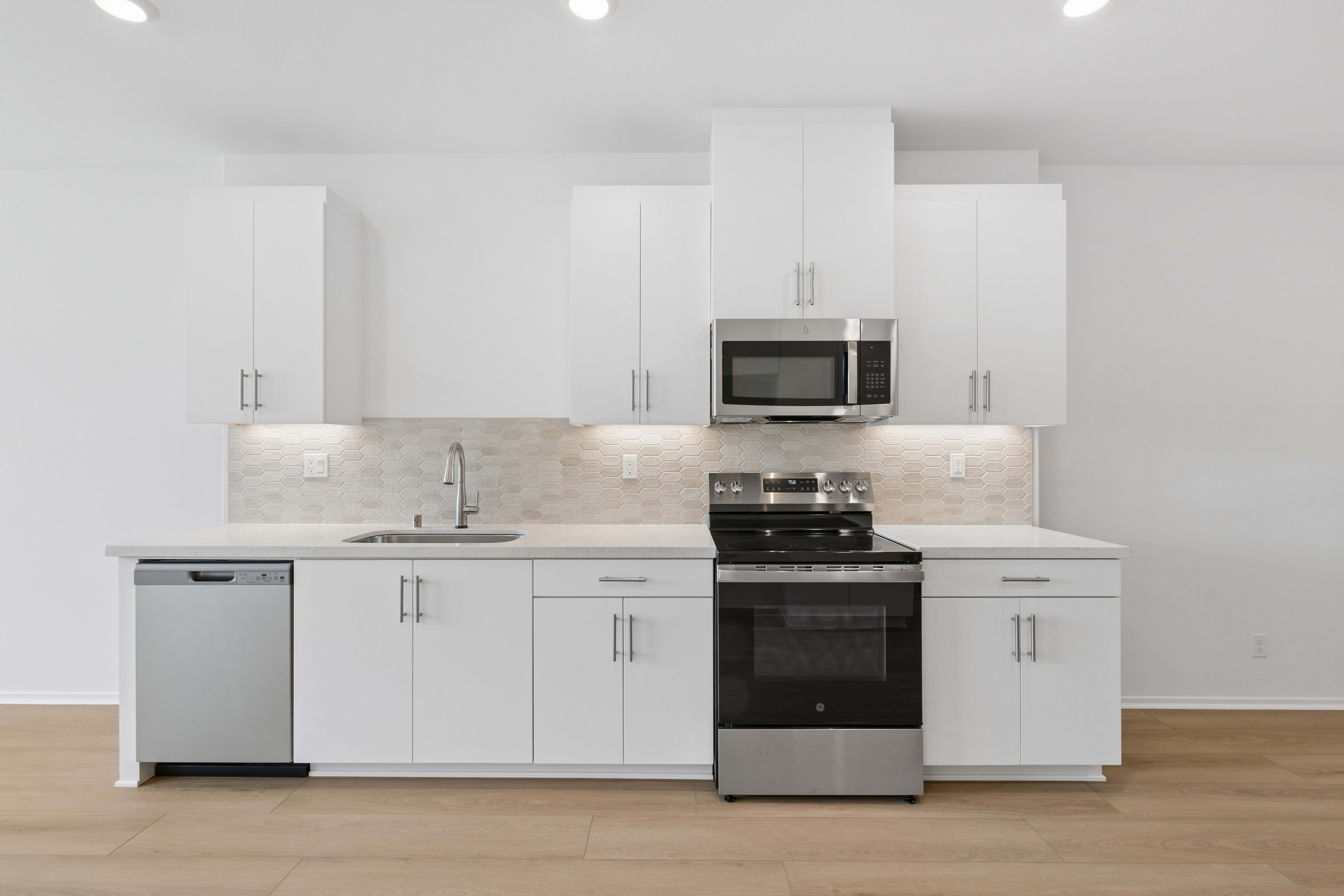 A modern, minimalist kitchen with white cabinets, stainless steel appliances, and a marble backsplash, set against a bright, airy background.