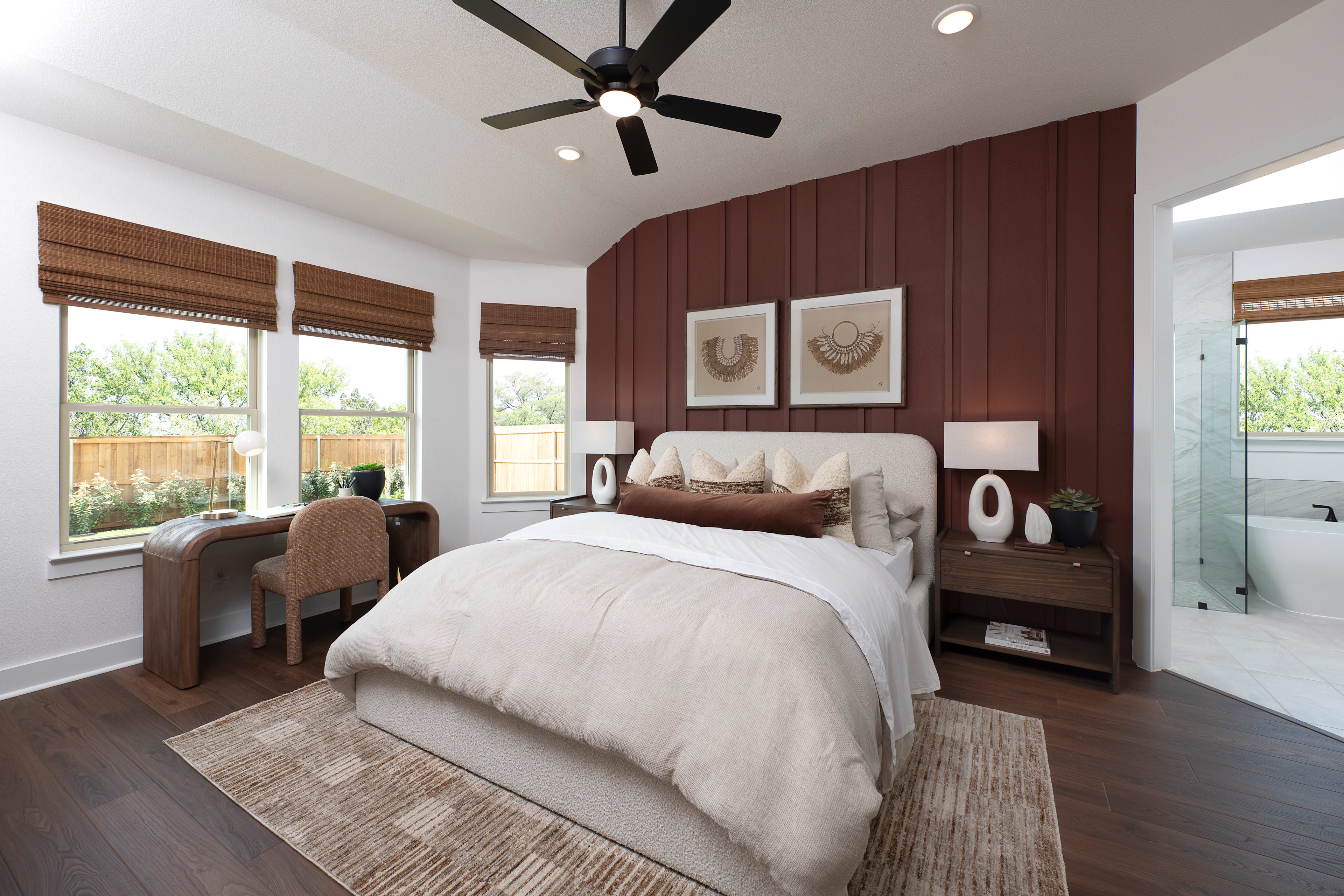 A cozy and well-furnished bedroom with a large bed, wooden paneled walls, and a ceiling fan, surrounded by large windows providing a view of the outdoor scenery.