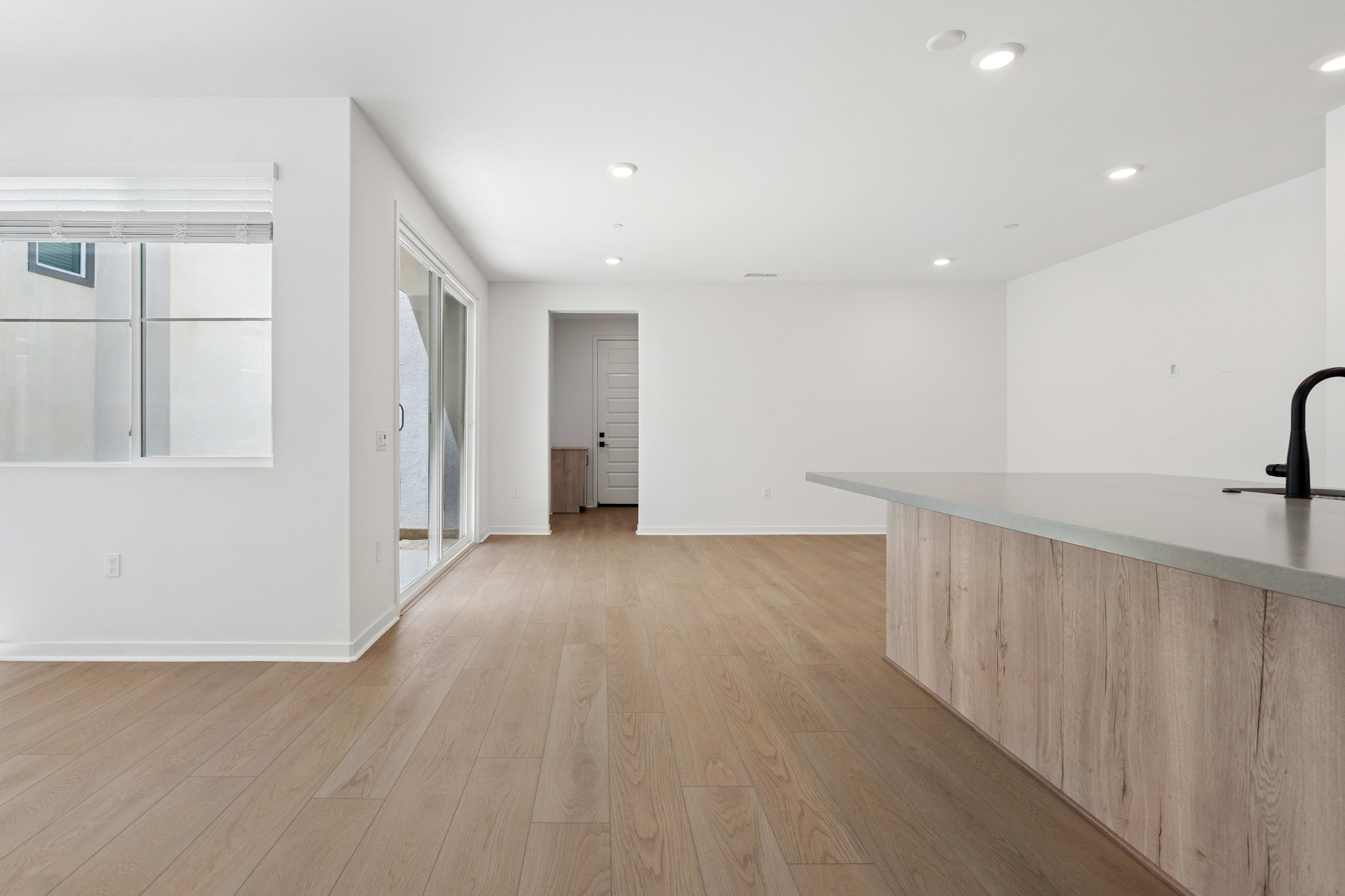 A spacious, minimalist interior with a wooden kitchen counter and hardwood floors, leading to a hallway with a door visible in the background.
