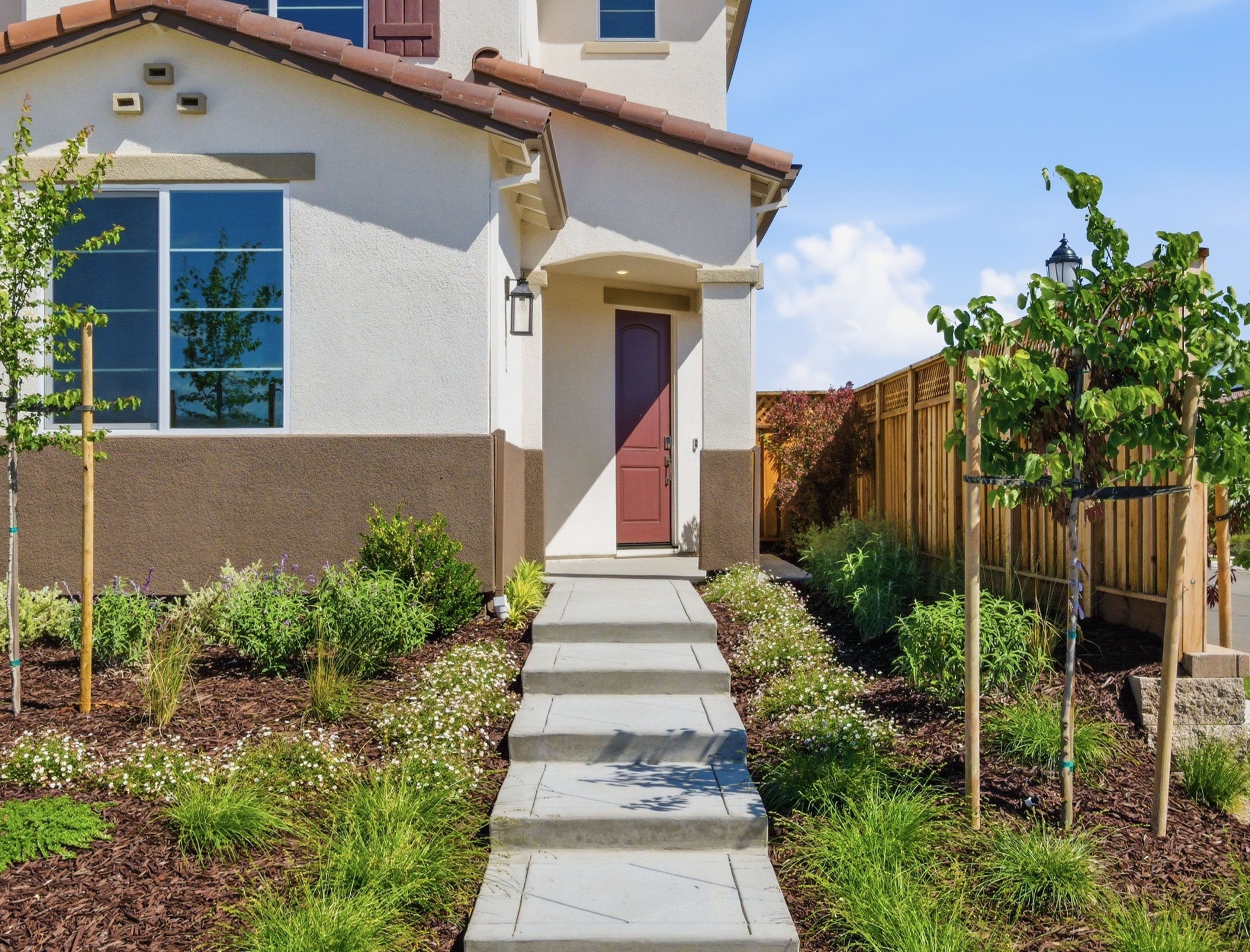 A well-maintained two-story house with a tiled roof, surrounded by a landscaped yard featuring a paved walkway and lush greenery.