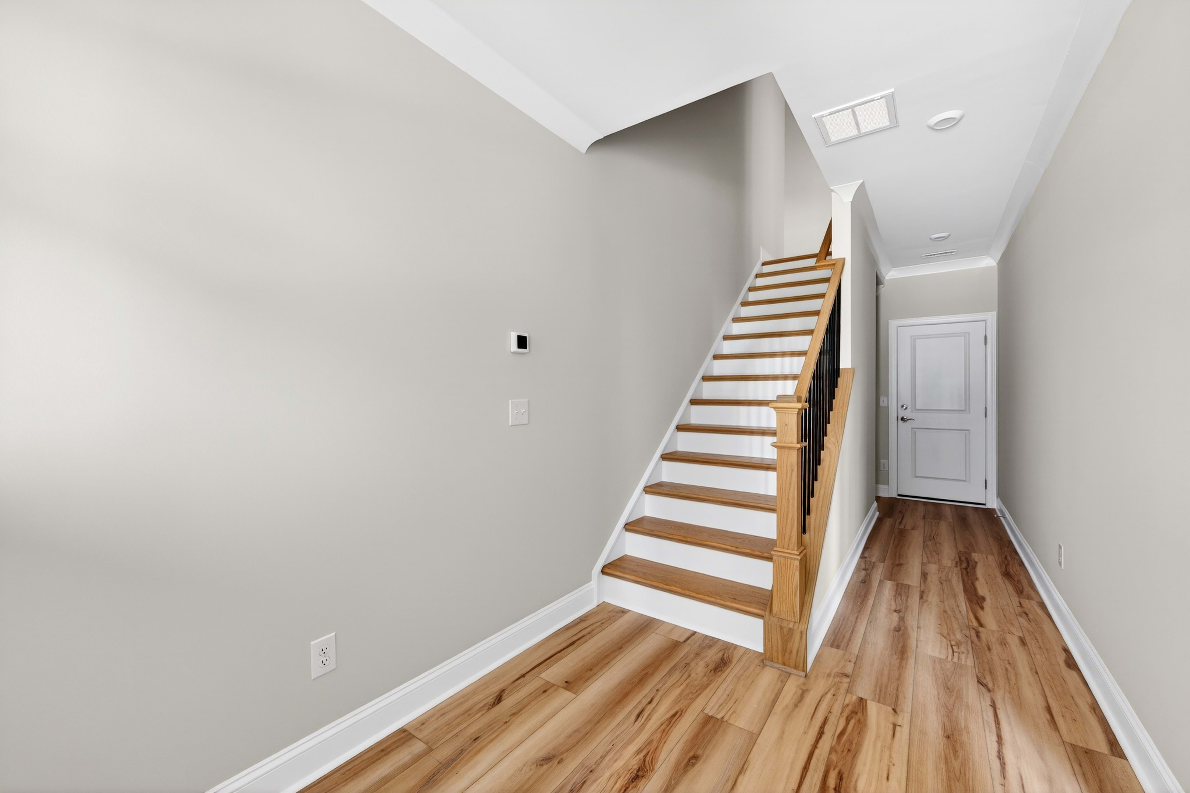 A bright and spacious hallway with a wooden staircase leading up, and a wooden floor extending into the background.