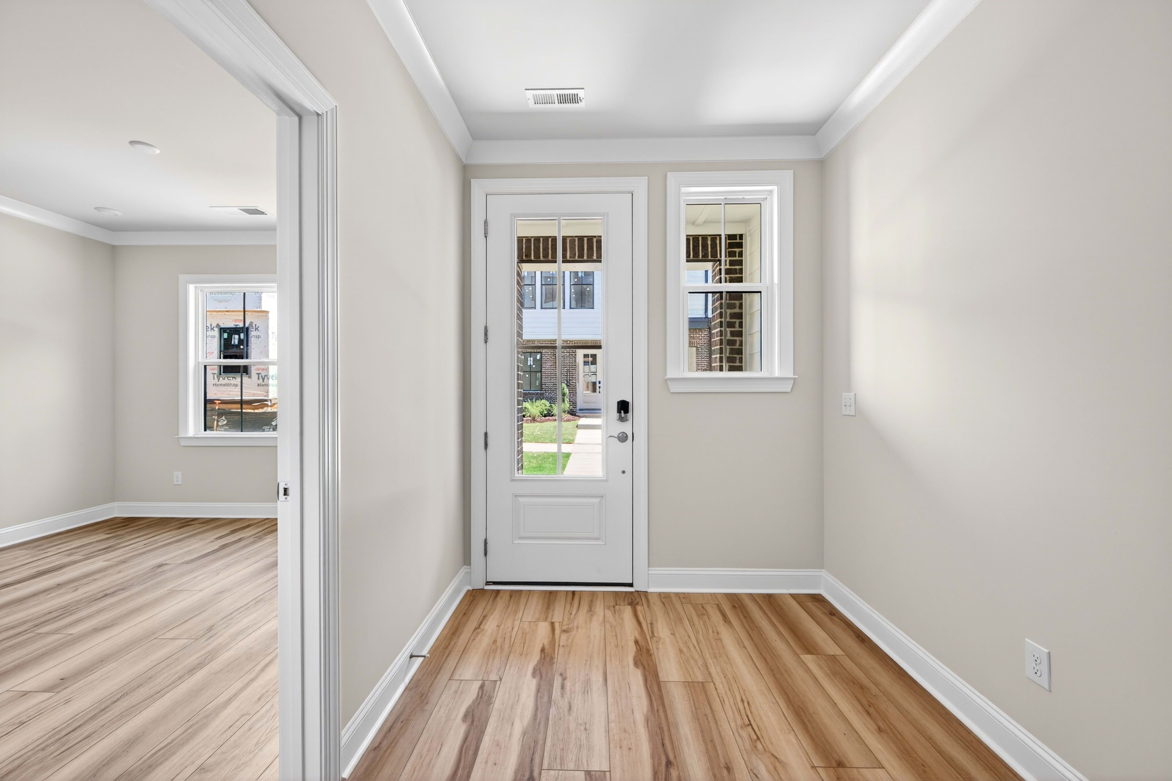 A bright and airy hallway with a wooden floor, white walls, and a glass-paneled door leading to the outdoors.