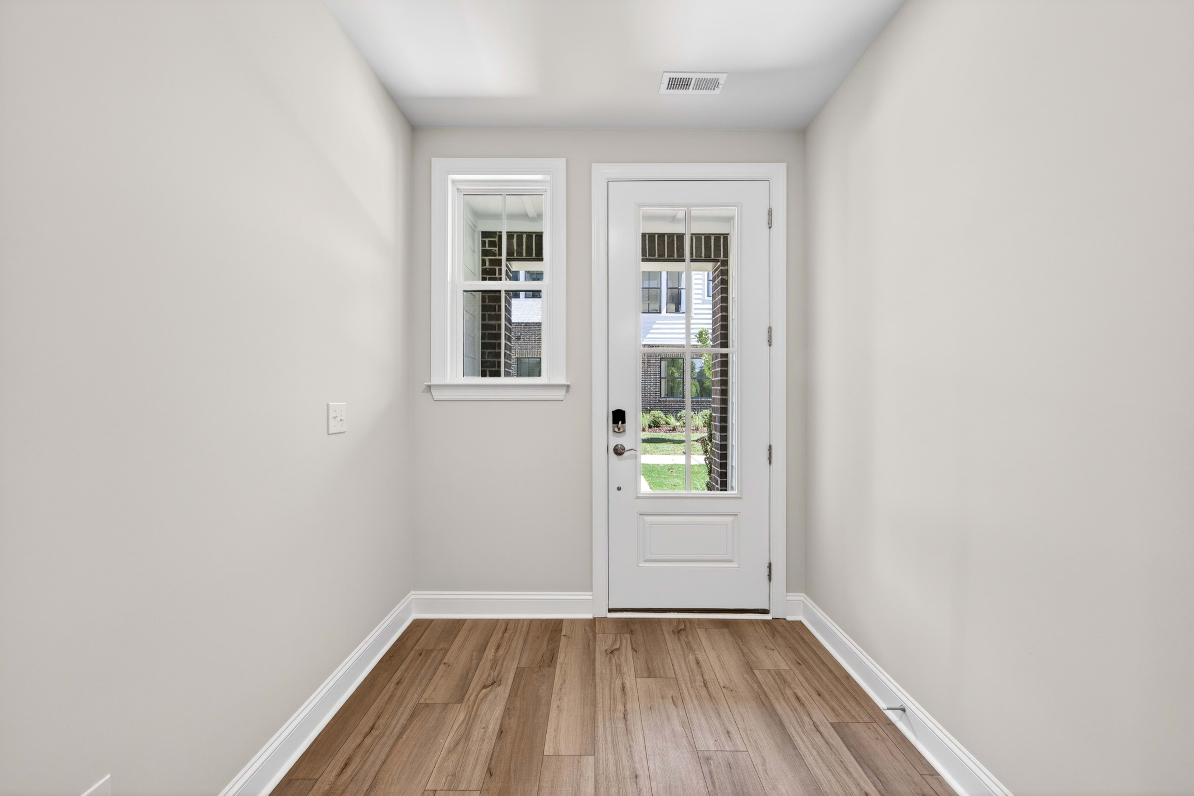 A bright, minimalist entryway with a white door leading to a view of the outdoors, and a hardwood floor extending through the space.