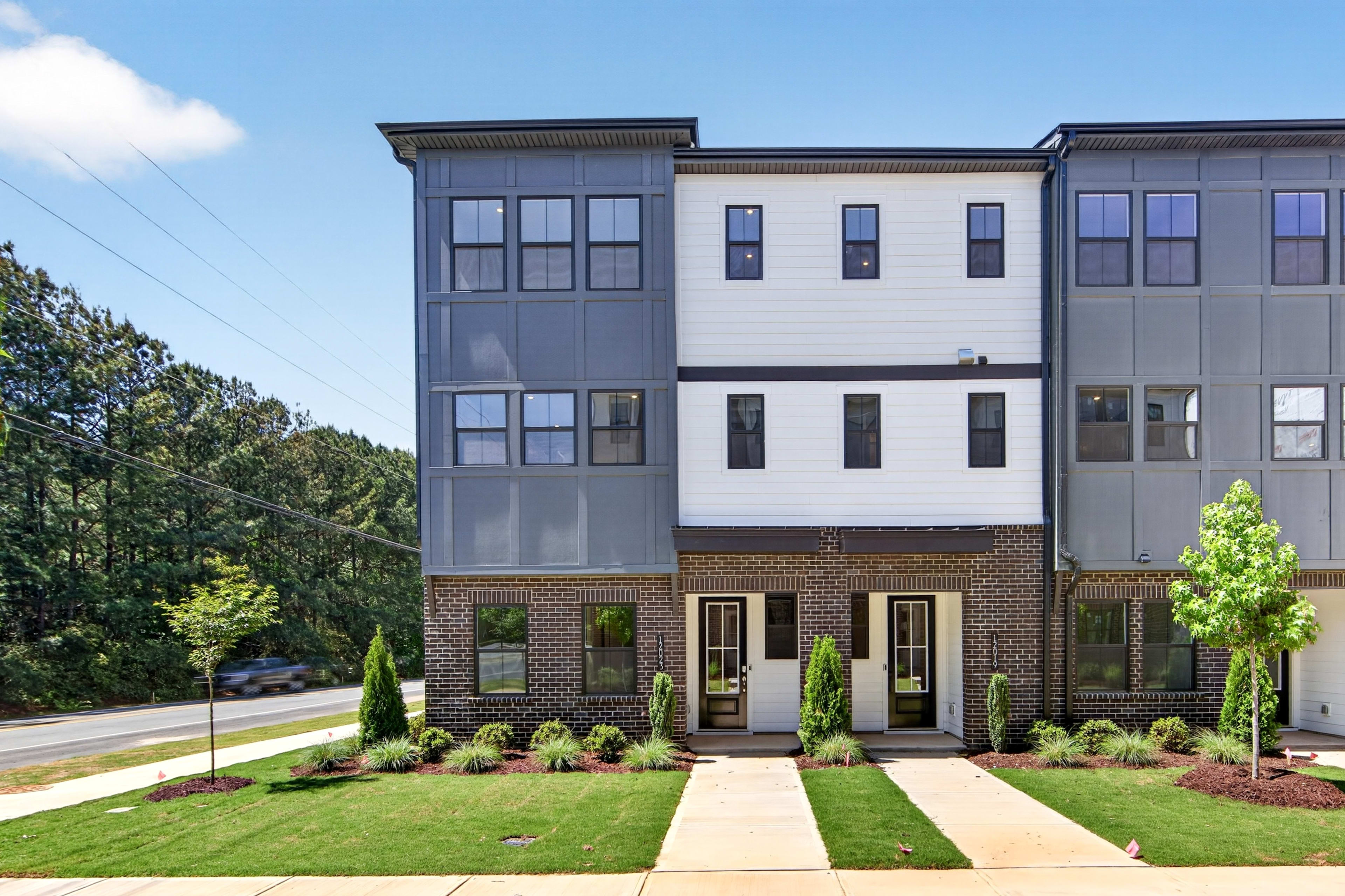 A multi-story residential building with a brick and siding exterior, surrounded by landscaped greenery and a paved walkway in the foreground.