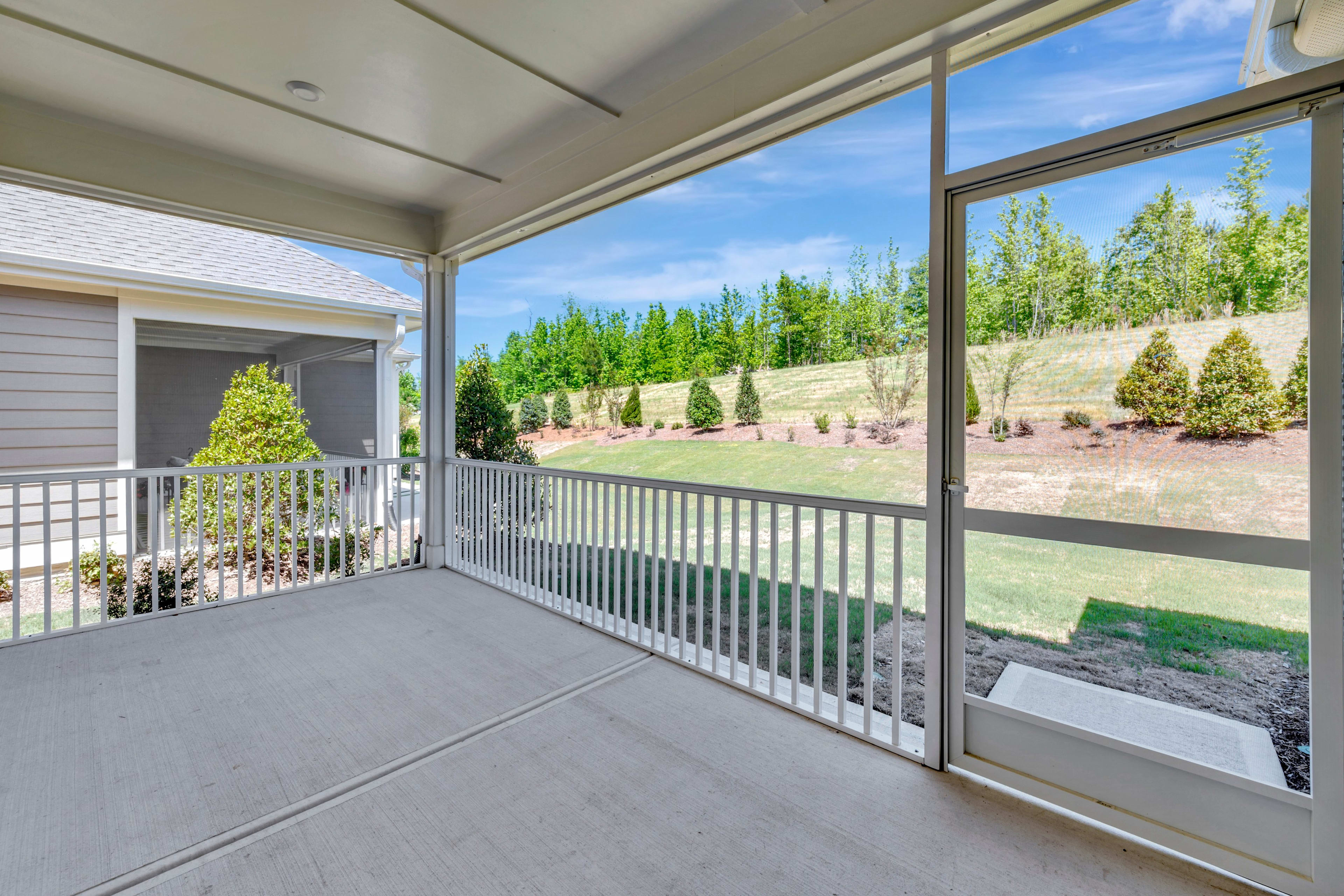 A covered patio with a railing overlooks a lush, green landscape with trees and shrubs in the background.