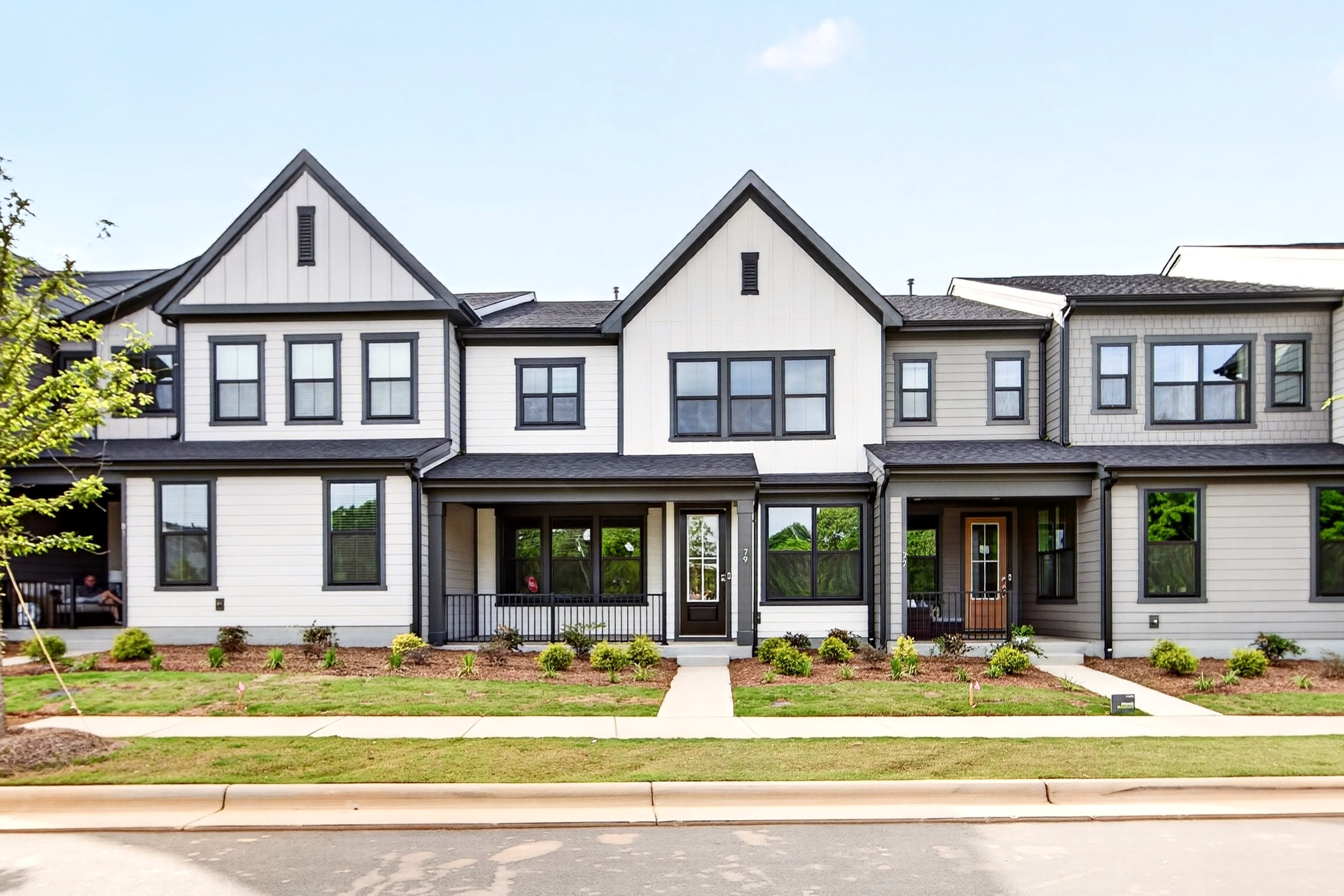 A row of modern townhouses with manicured lawns in the foreground stands against a clear blue sky.
