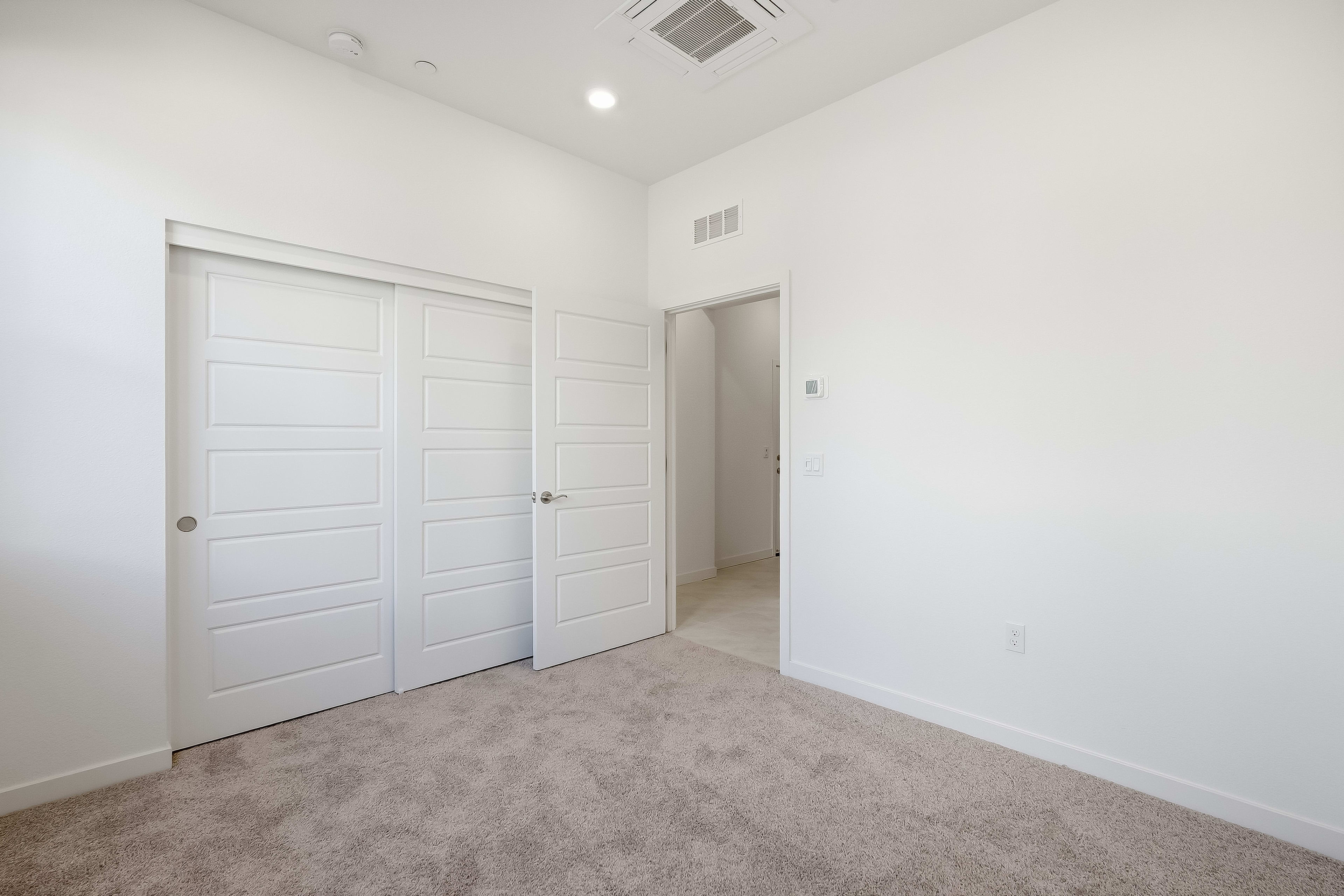 A carpeted floor fills the foreground, leading to a wall with two closed closet doors and an open doorway in the background.