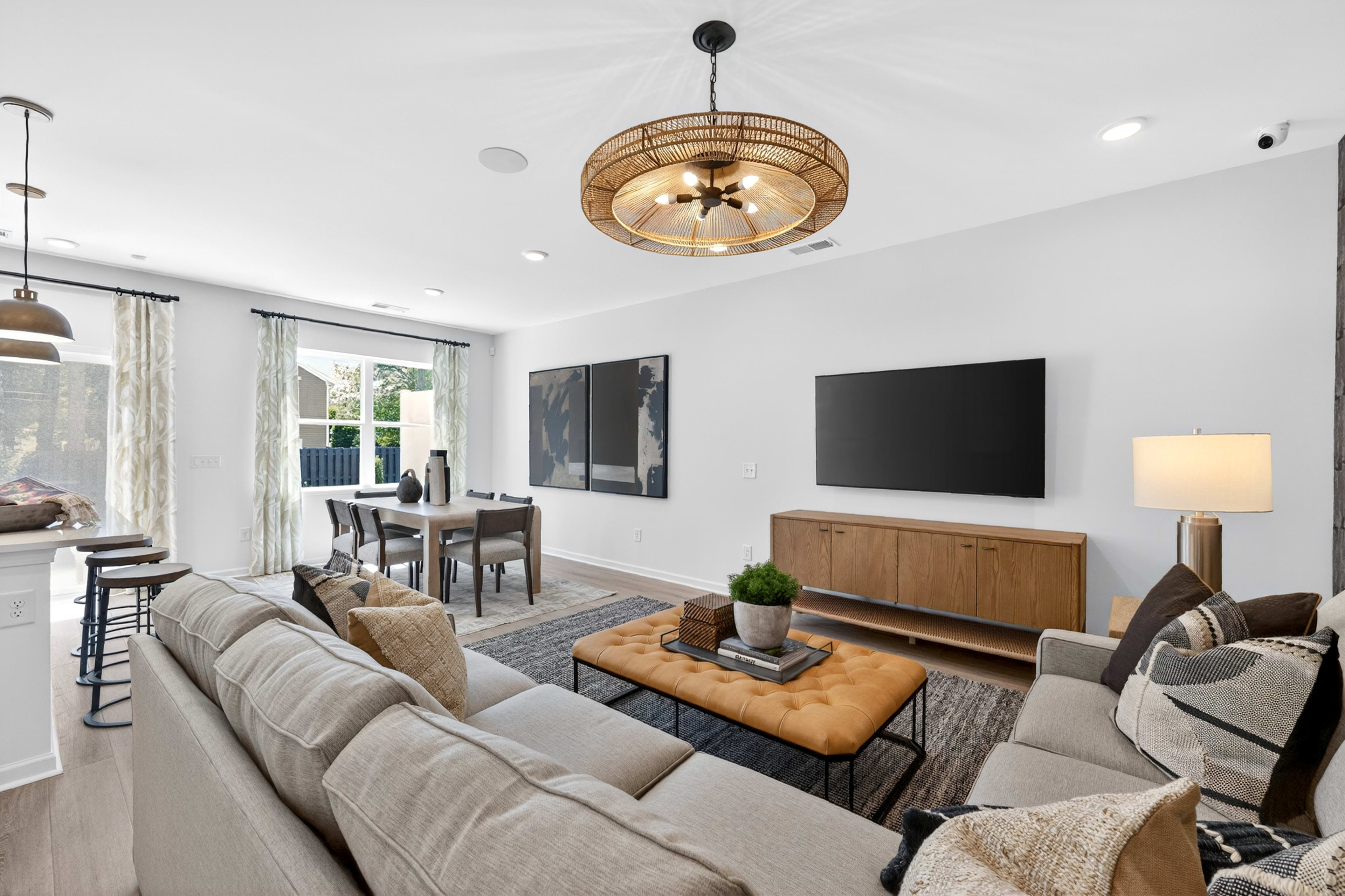A spacious living room with a large sectional sofa and ottoman in the foreground, and a dining area with a table and chairs visible in the background.