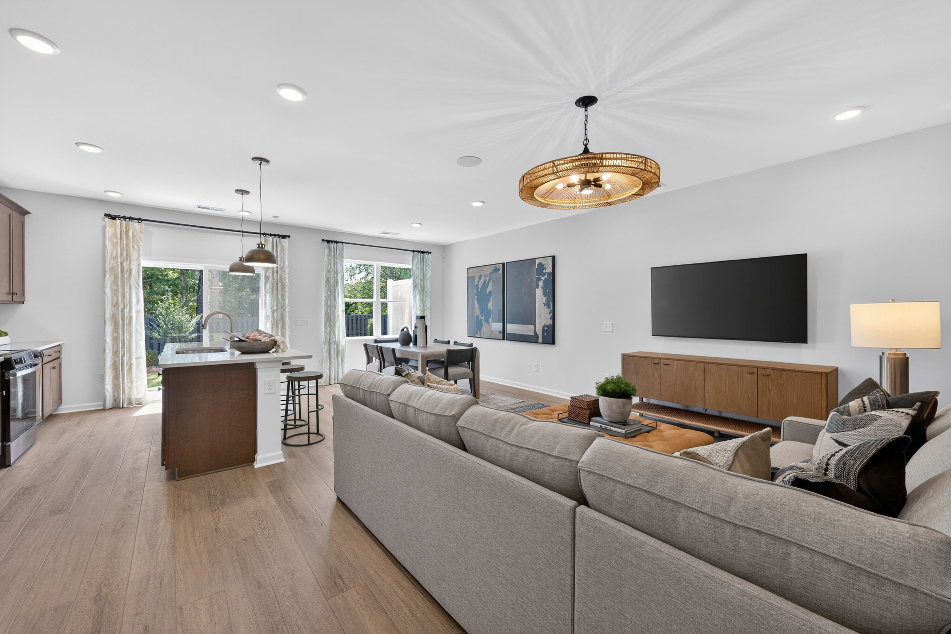 A spacious, modern living and dining area with a large sectional sofa in the foreground and a dining table and kitchen island in the background.
