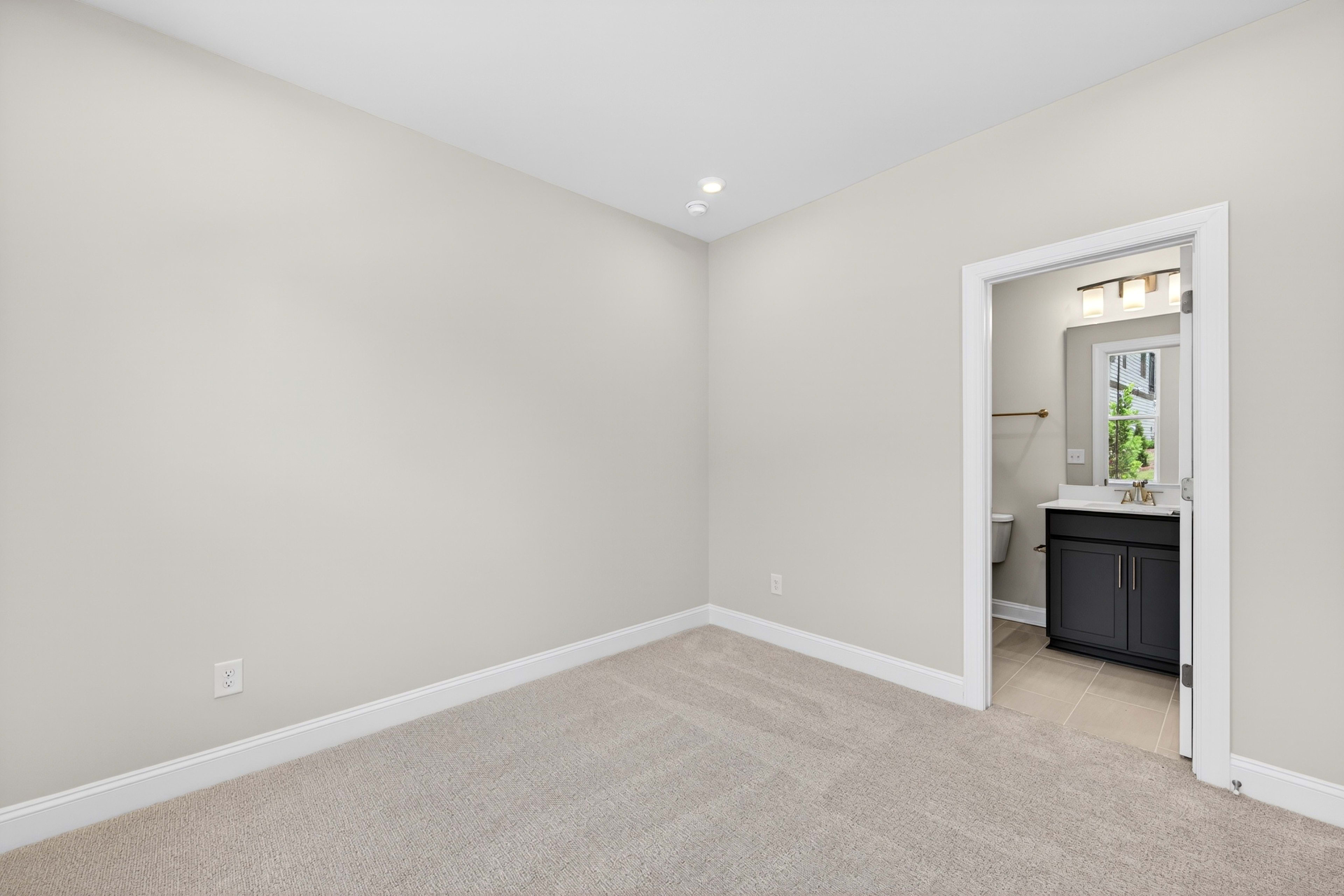 A carpeted room with a doorway opening to a bathroom with a vanity and toilet.